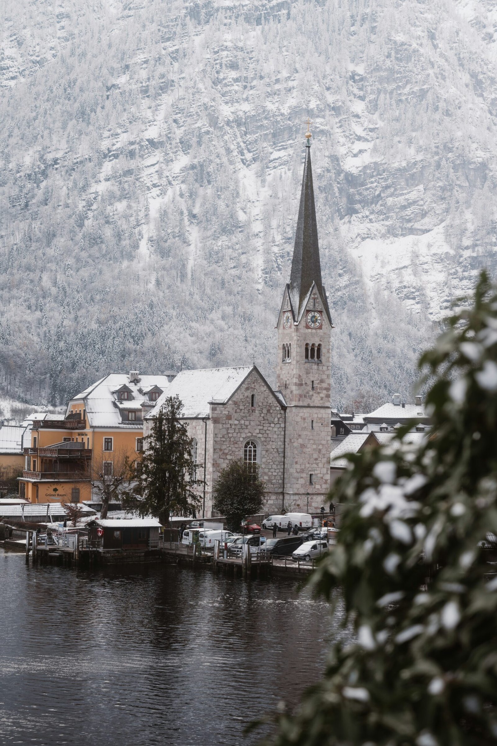 Hallstatt waterfront in winter with a church spire, snowy rooftops, and calm alpine water.