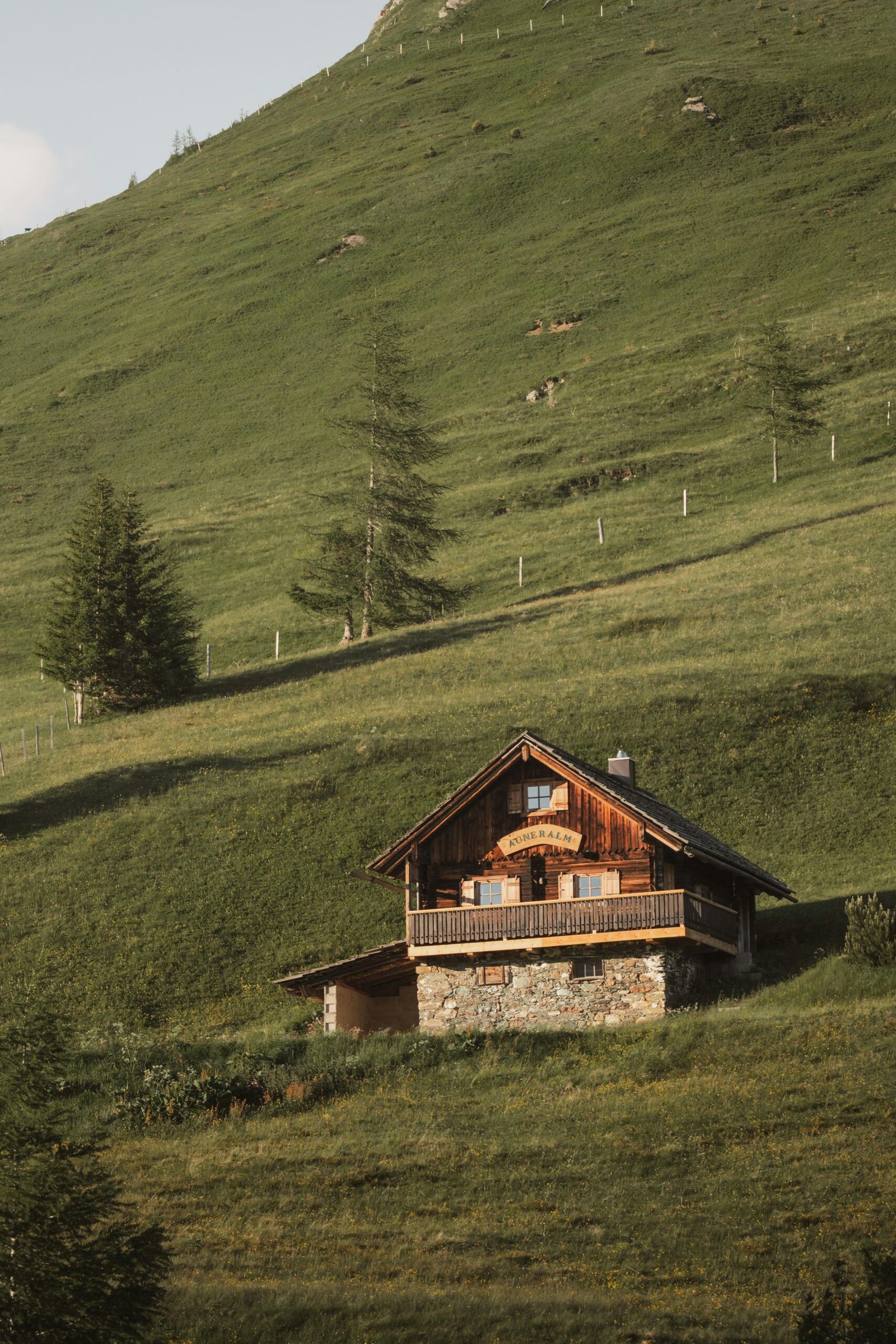 A secluded wooden alpine cabin on a lush green mountainside, representing the quiet solitude and remote locations of luxury digital detox retreats.