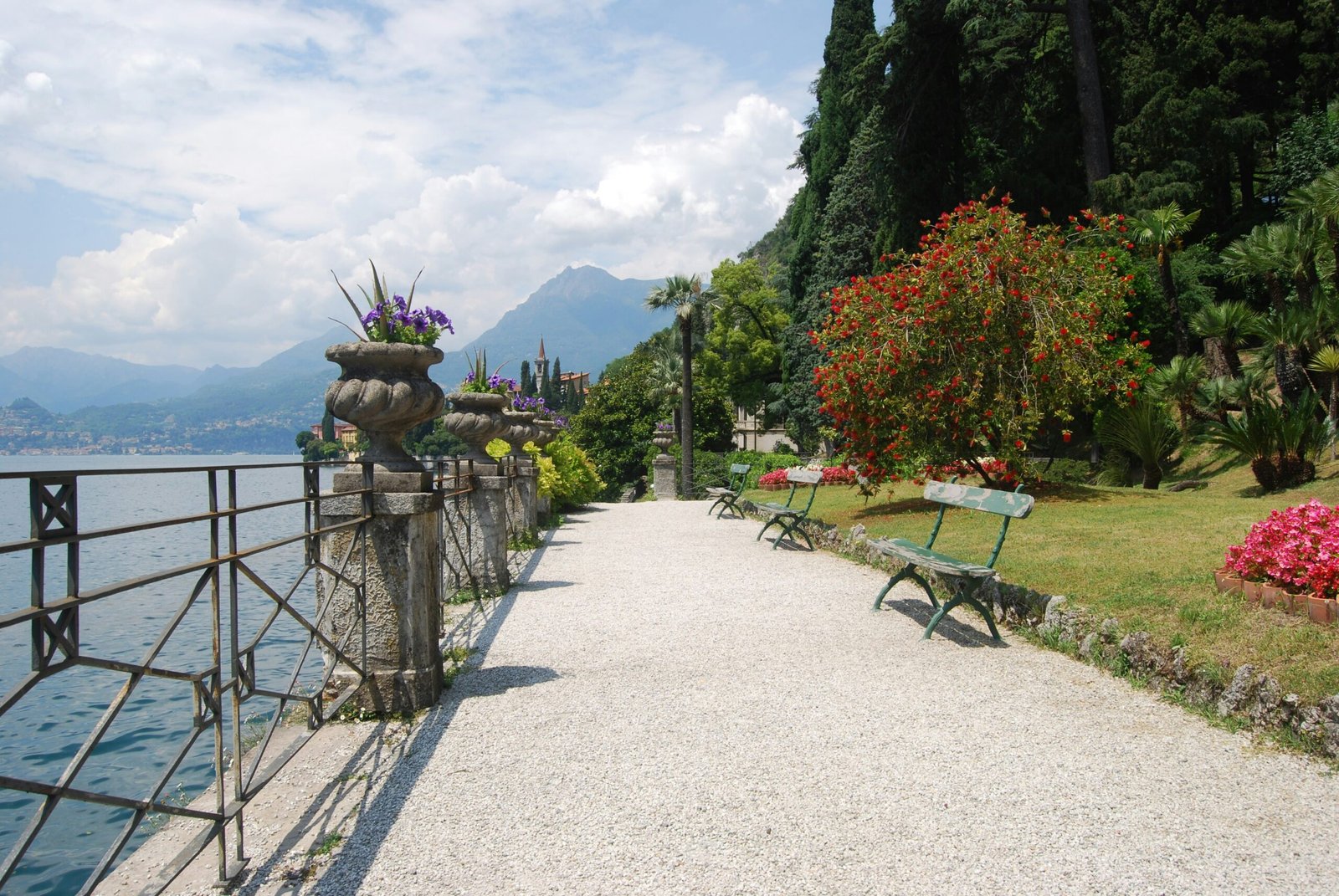 Botanical garden path at Lake Como with spring flowers beside calm water in Italy.