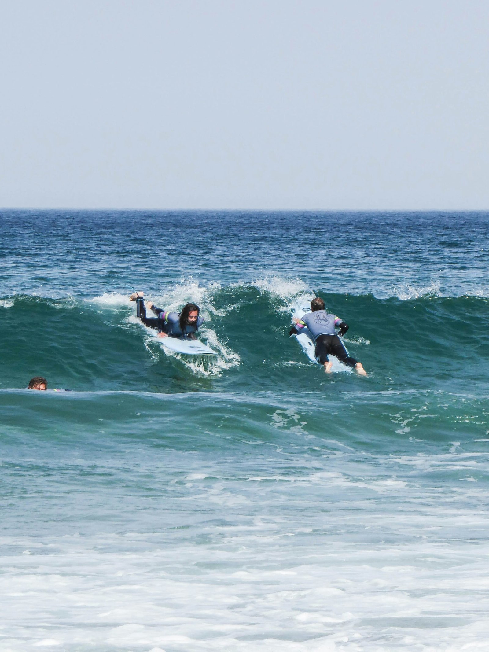 Two surfers catching a wave together in the bright blue waters of Ericeira, showcasing the community and active wellness atmosphere of a Portuguese surf and yoga retreat.