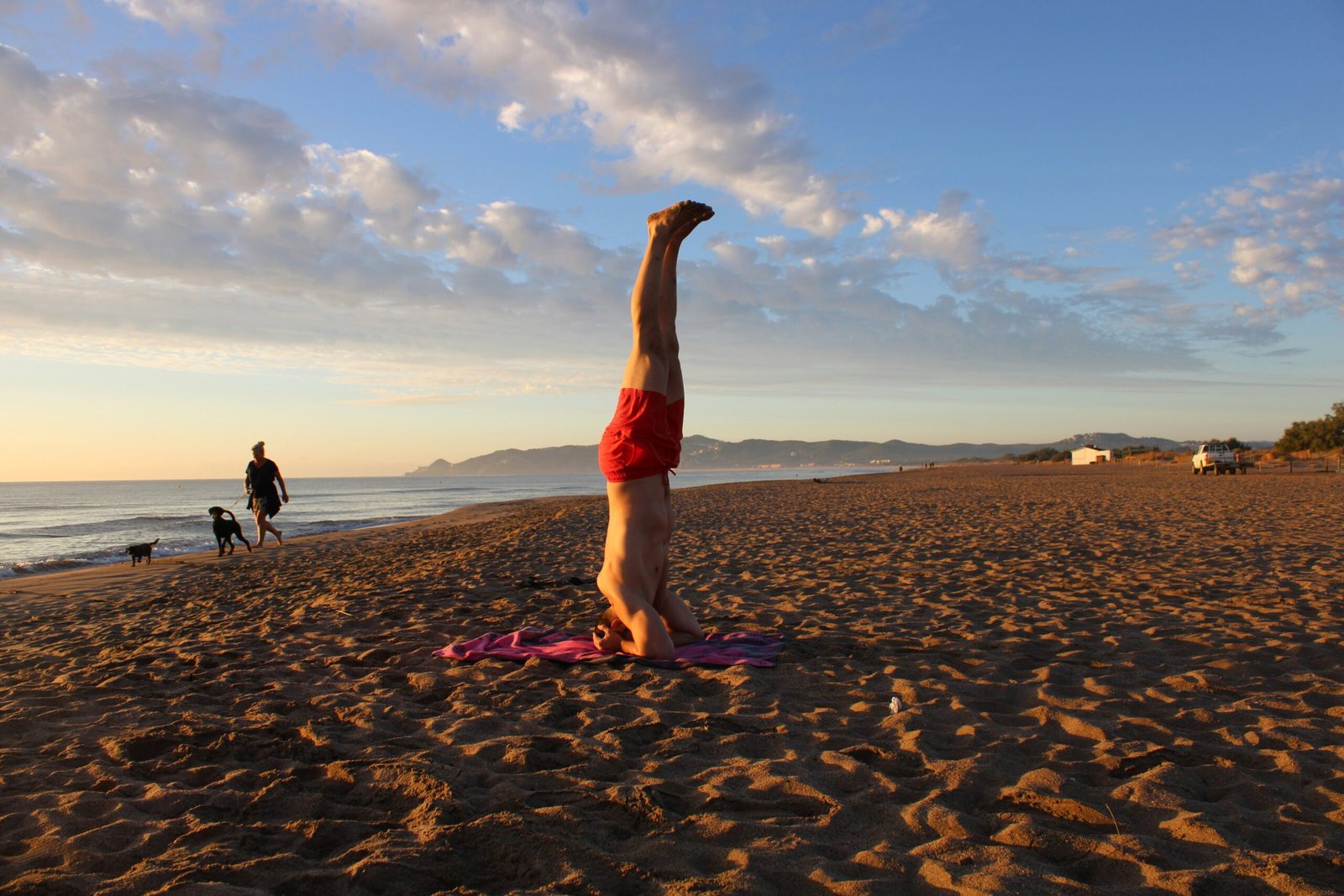 A man performing a headstand on a yoga mat at sunset on a wide sandy beach in Spain, symbolizing the balance and focus of a surf and yoga retreat.
