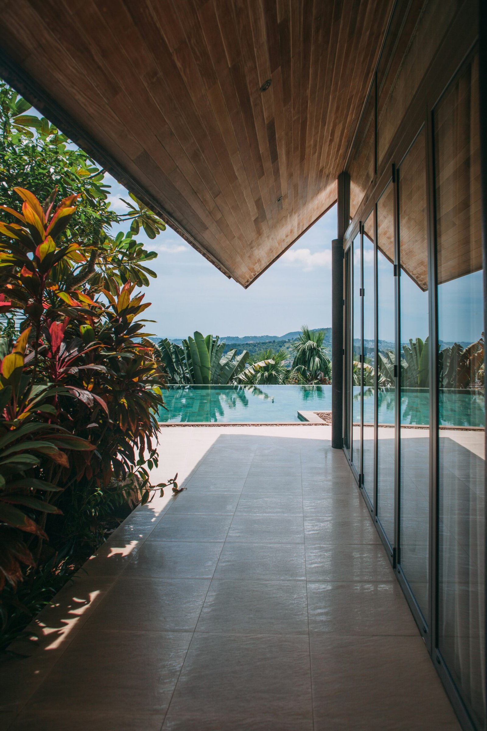 Modern walkway leading to an infinity pool framed by tropical plants in a serene resort setting.