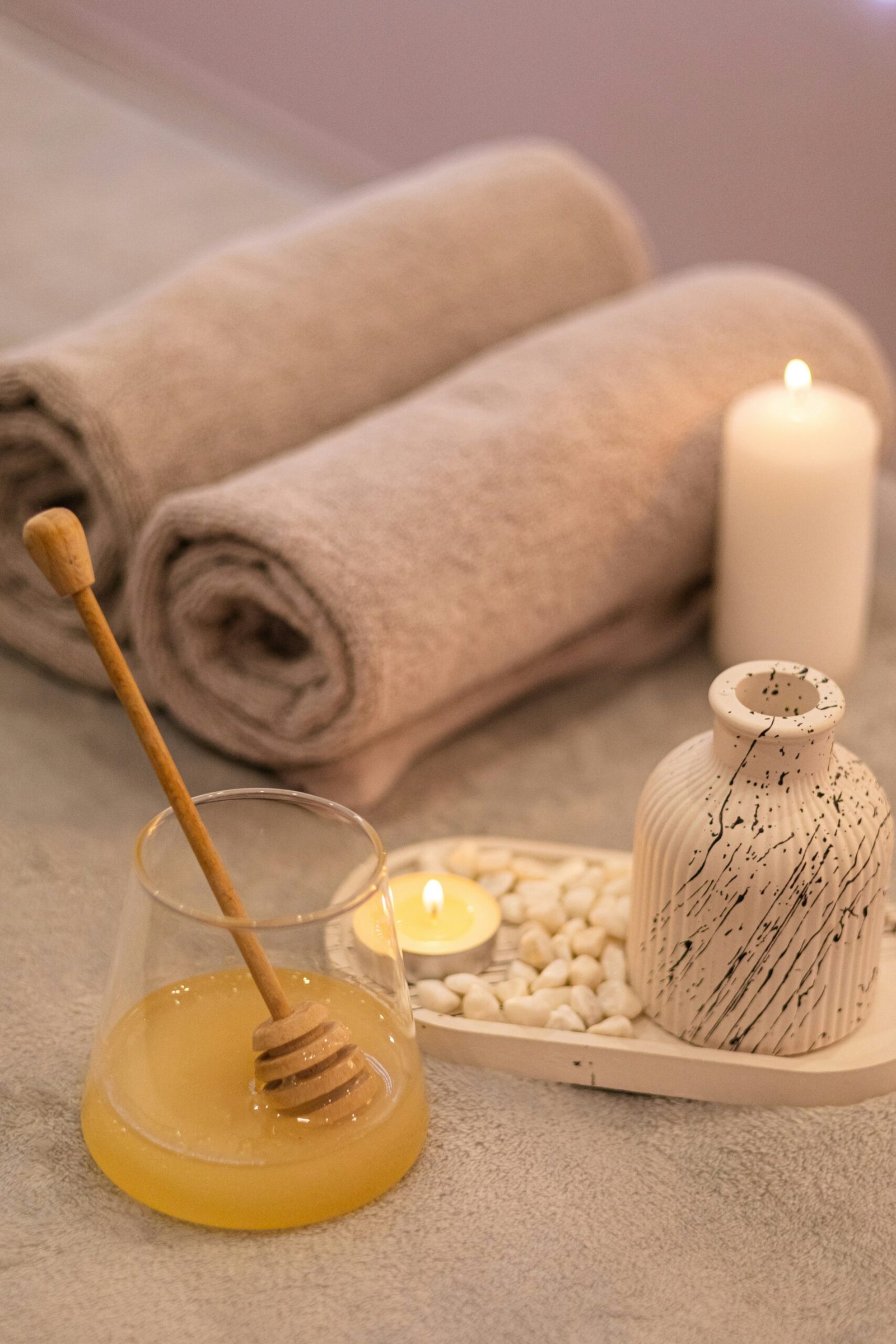 Candles, towels, and a jar of honey arranged in a spa-style setup for a soothing wellness retreat ritual.