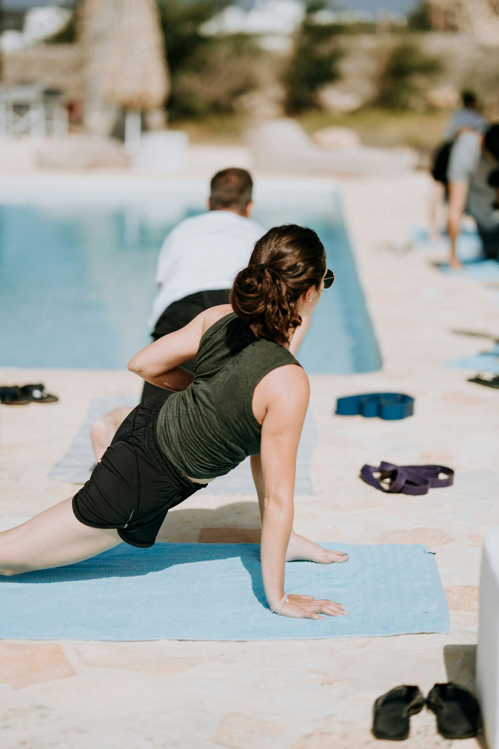A woman practicing a side lunge yoga pose on a blue mat by a resort pool, highlighting the combination of physical wellness and relaxation during a solo yoga retreat.