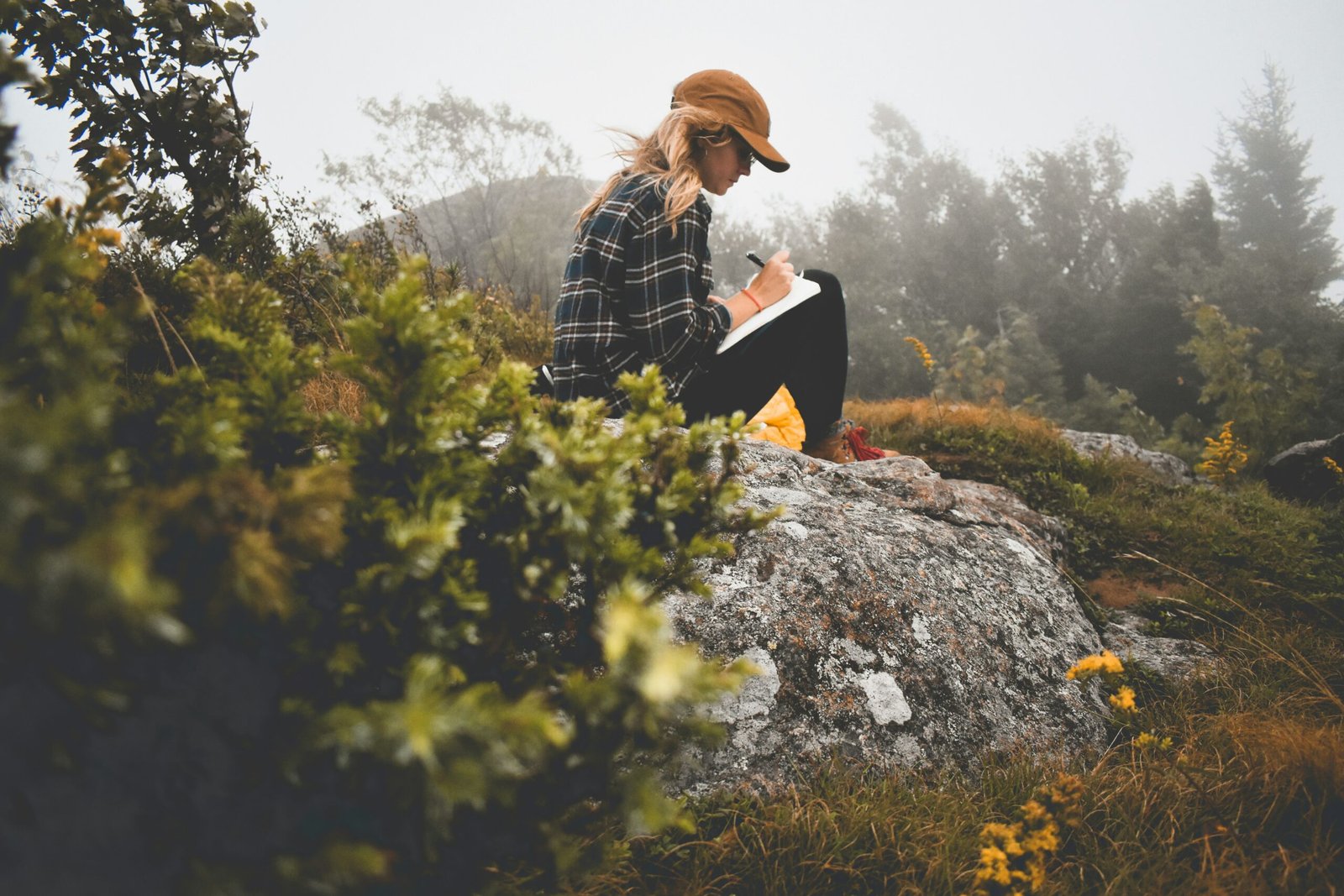 Woman journaling while seated on a rock in the Adirondack Mountains, creating a reflective wellness scene.