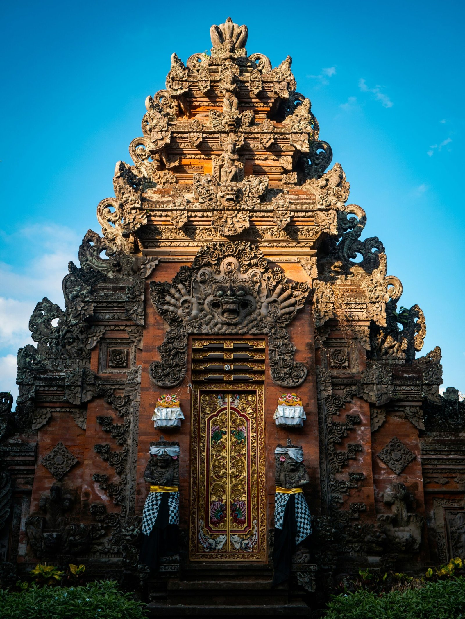 carved balinese temple gate after rain beneath a clear blue morning
