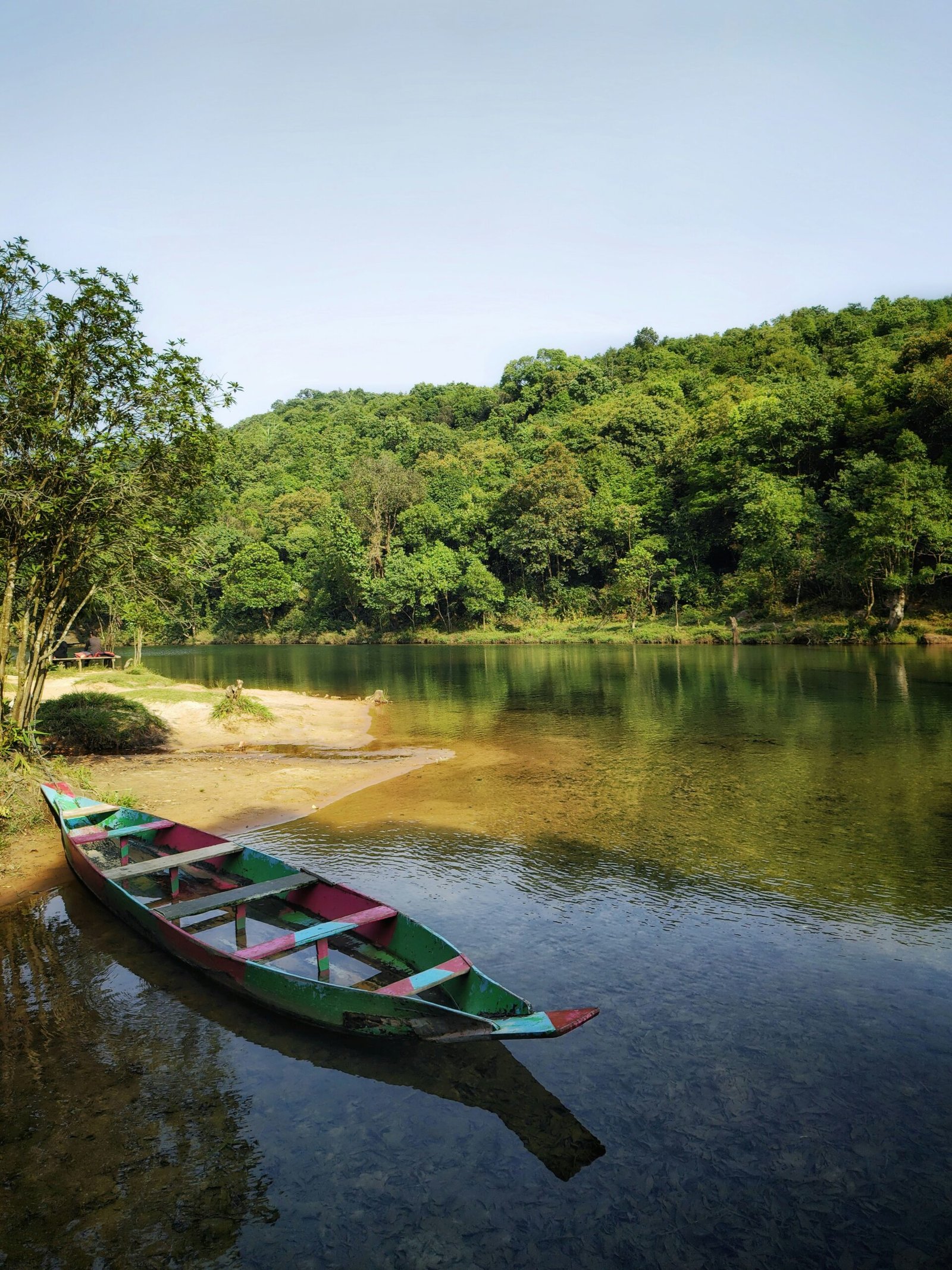 Canoe resting beside a clear forest lake near Krangshuri Waterfall in Meghalaya, reflecting the serene natural mood of a wellness retreat in India.