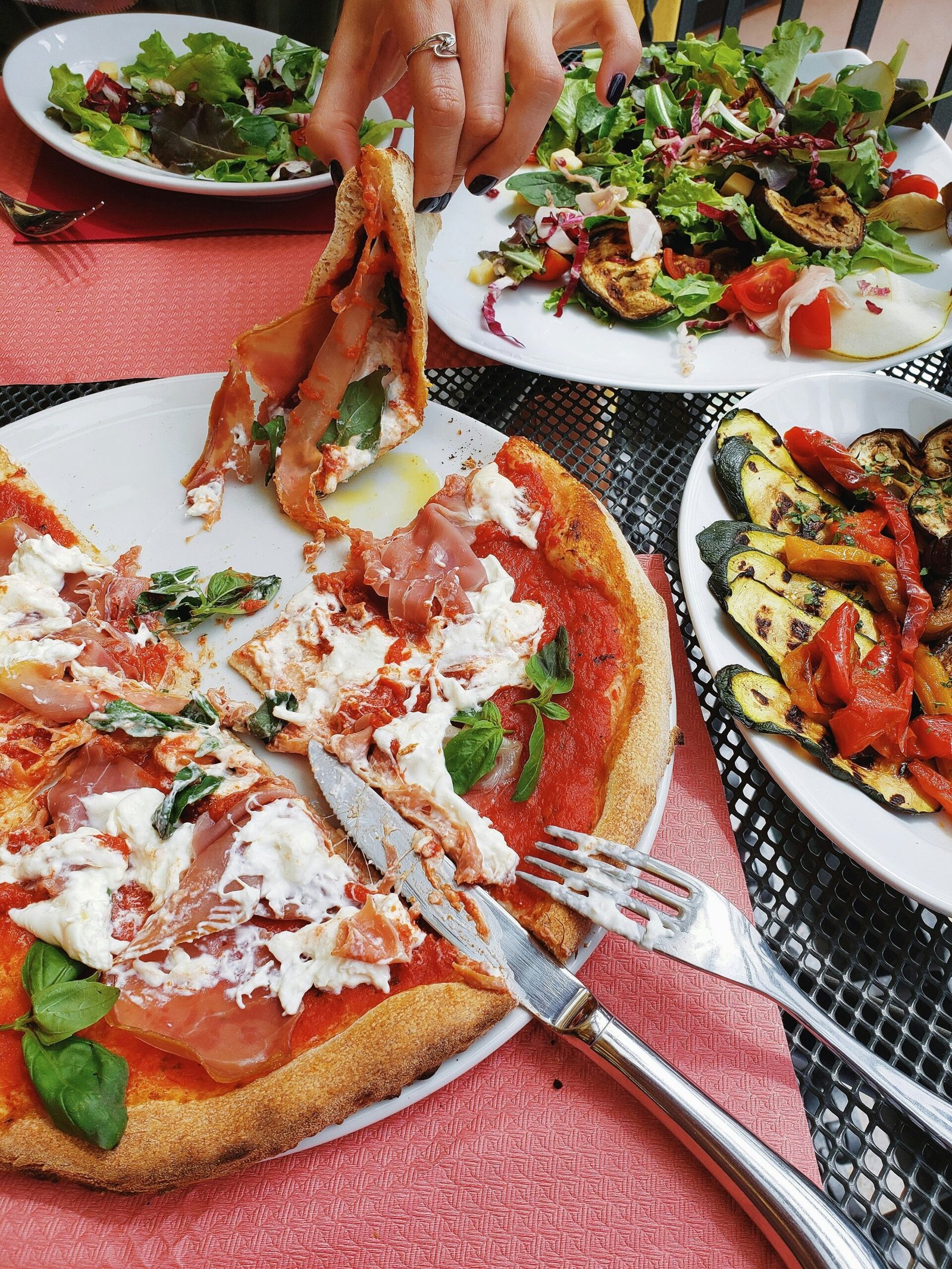 A vibrant table spread of Mediterranean food including a fresh burrata and prosciutto pizza, grilled vegetables, and seasonal salads, illustrating the art of slow nourishment.