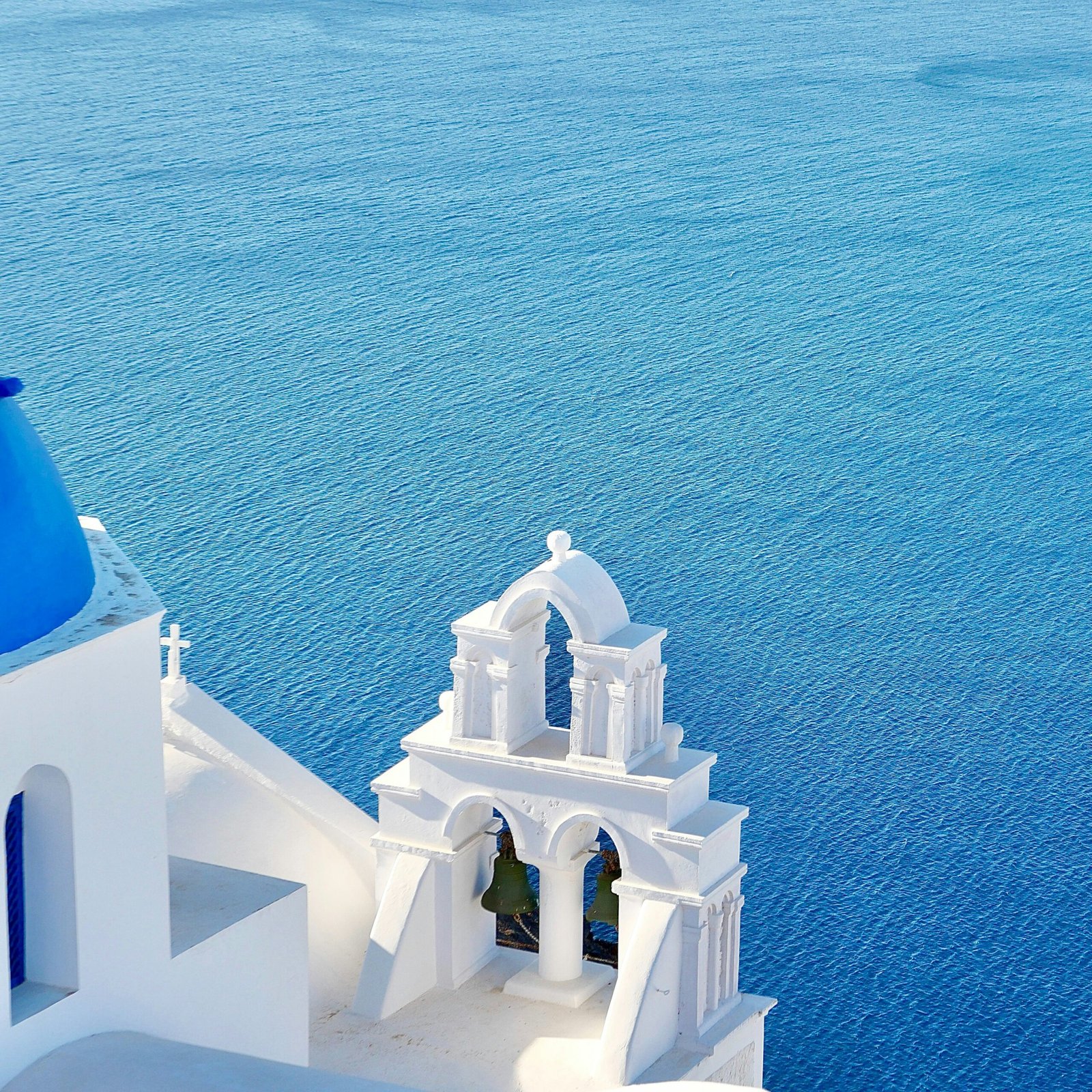 Blue-domed church in Oia, Santorini glowing in bright Mediterranean light.