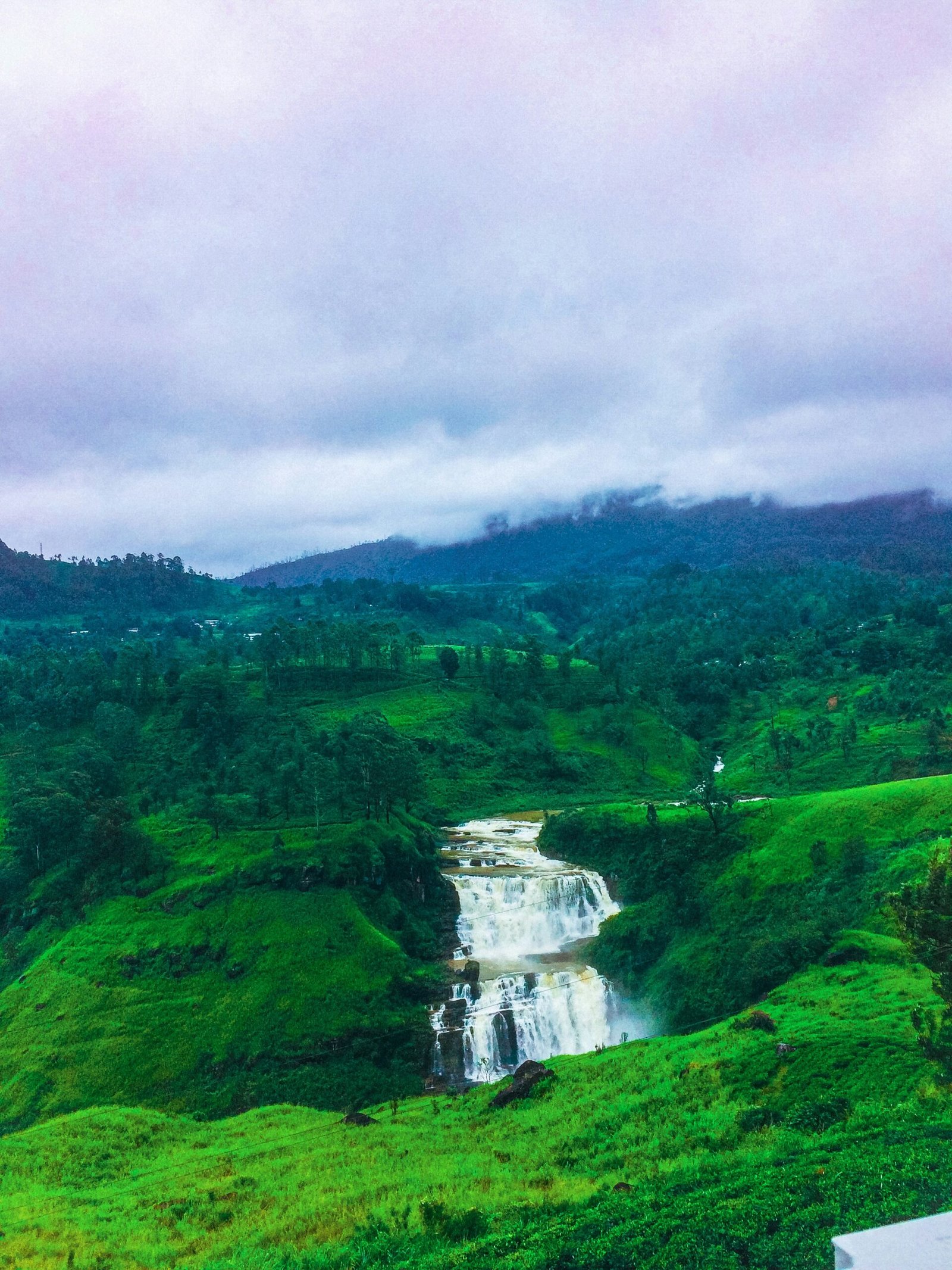 Lush Sri Lankan hillside with a distant waterfall reflecting the fresh natural energy of a March ayurveda retreat.