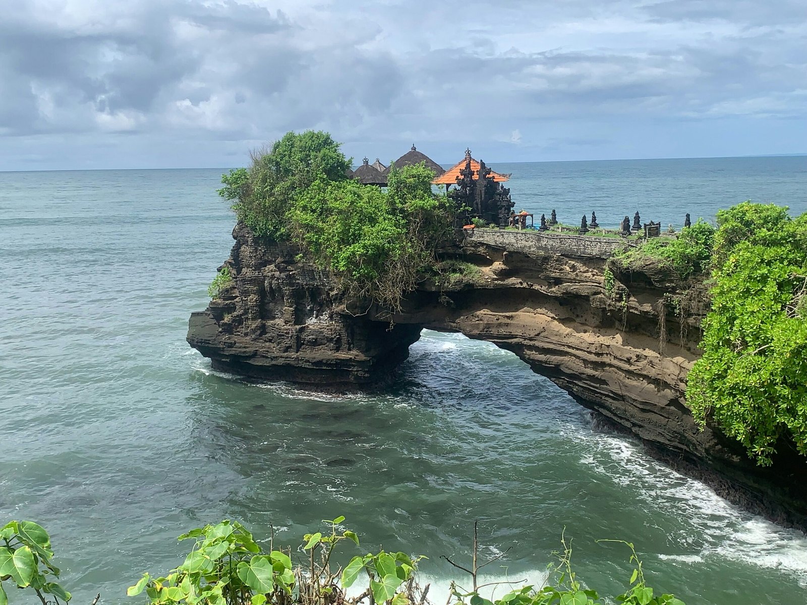 A wide-angle view of the Uluwatu temple stone pathway winding along a high limestone cliff overlooking the Indian Ocean, perfect for a Spring 2026 sunset yoga retreat in Bali.