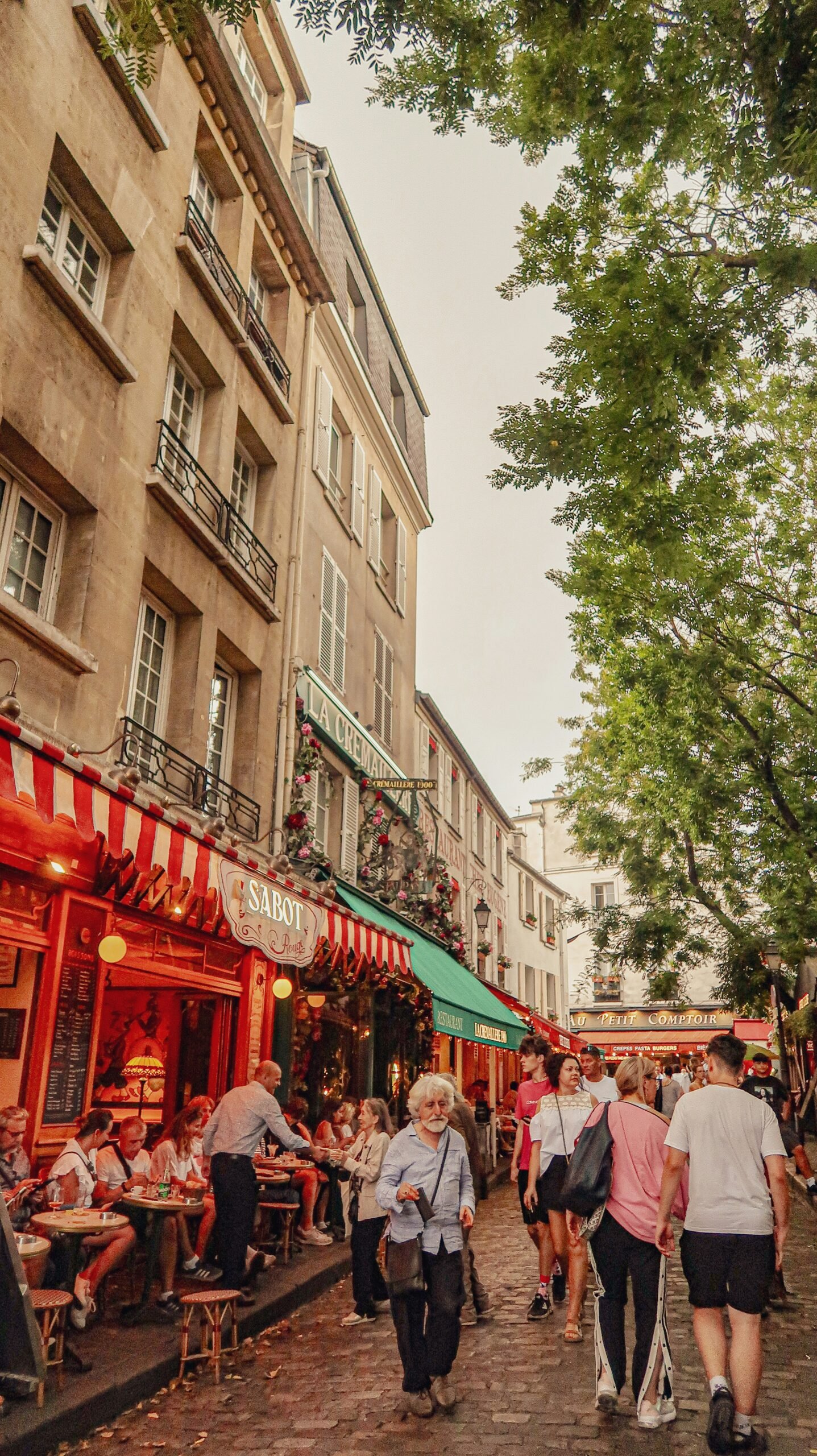 Cafe-lined Montmartre street in Paris with people strolling on a warm afternoon