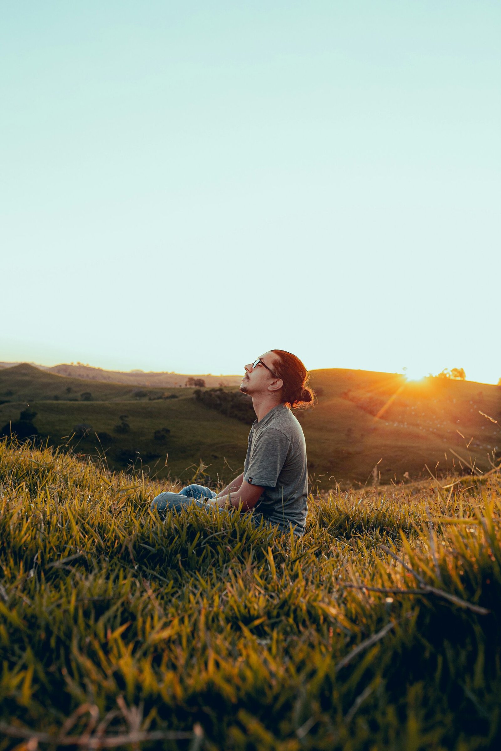A man practicing mindful breathing on a grassy hill at sunset, demonstrating how to integrate meditation into daily life after a wellness retreat.