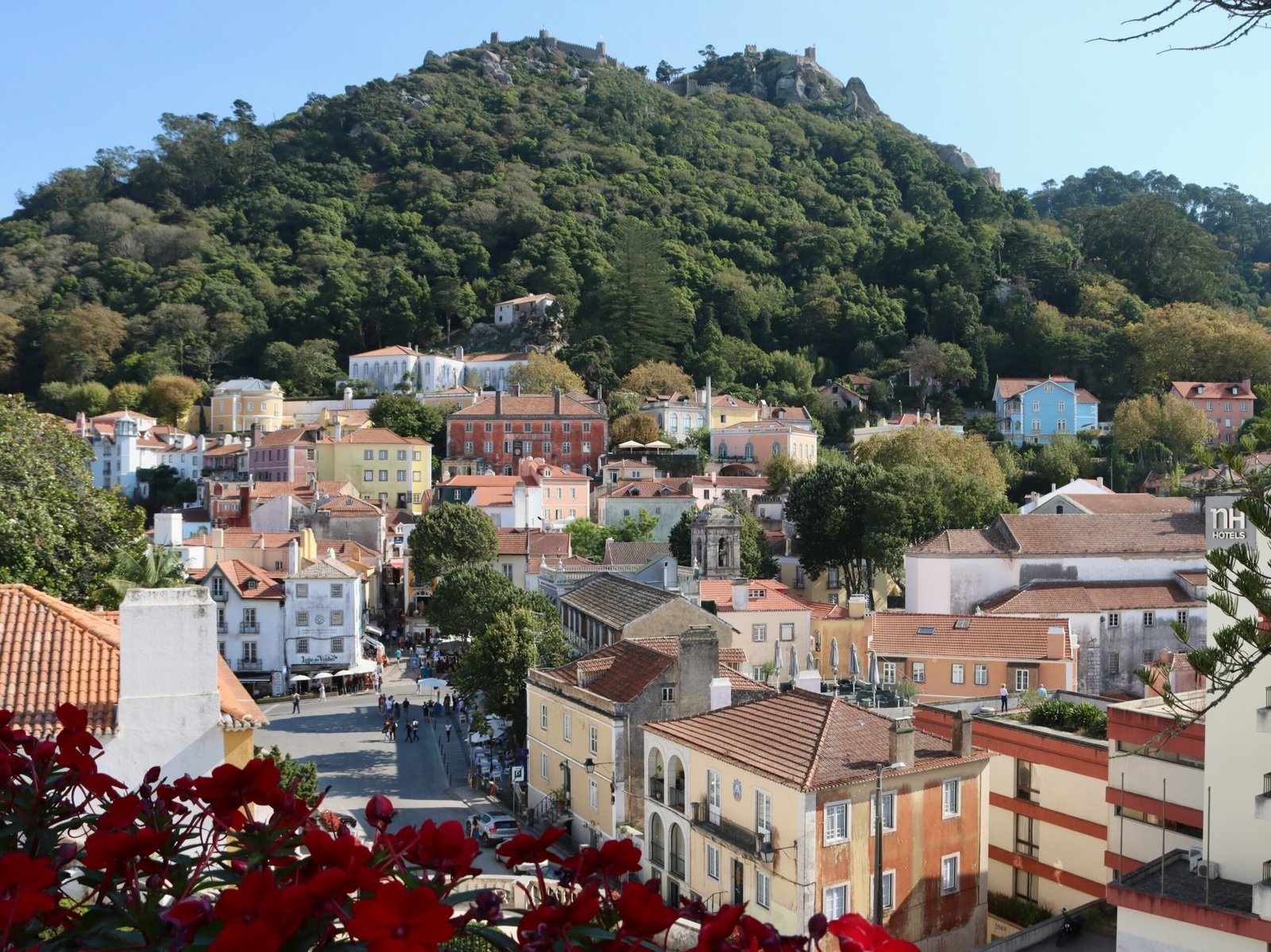 A panoramic view of the colorful historic center of Sintra, Portugal, nestled at the foot of lush green mountains with a medieval castle on the peak, ideal for a spiritual spring yoga retreat.