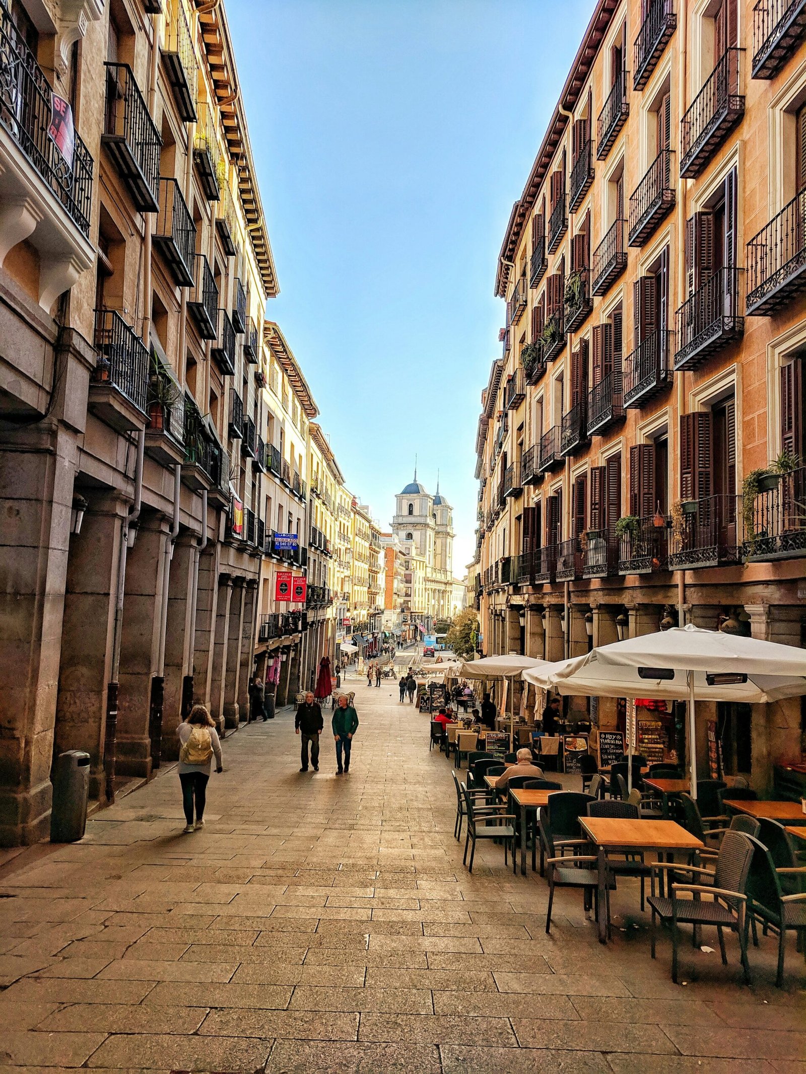 People walking through Plaza Mayor in Madrid, Spain, under a bright blue daytime sky.