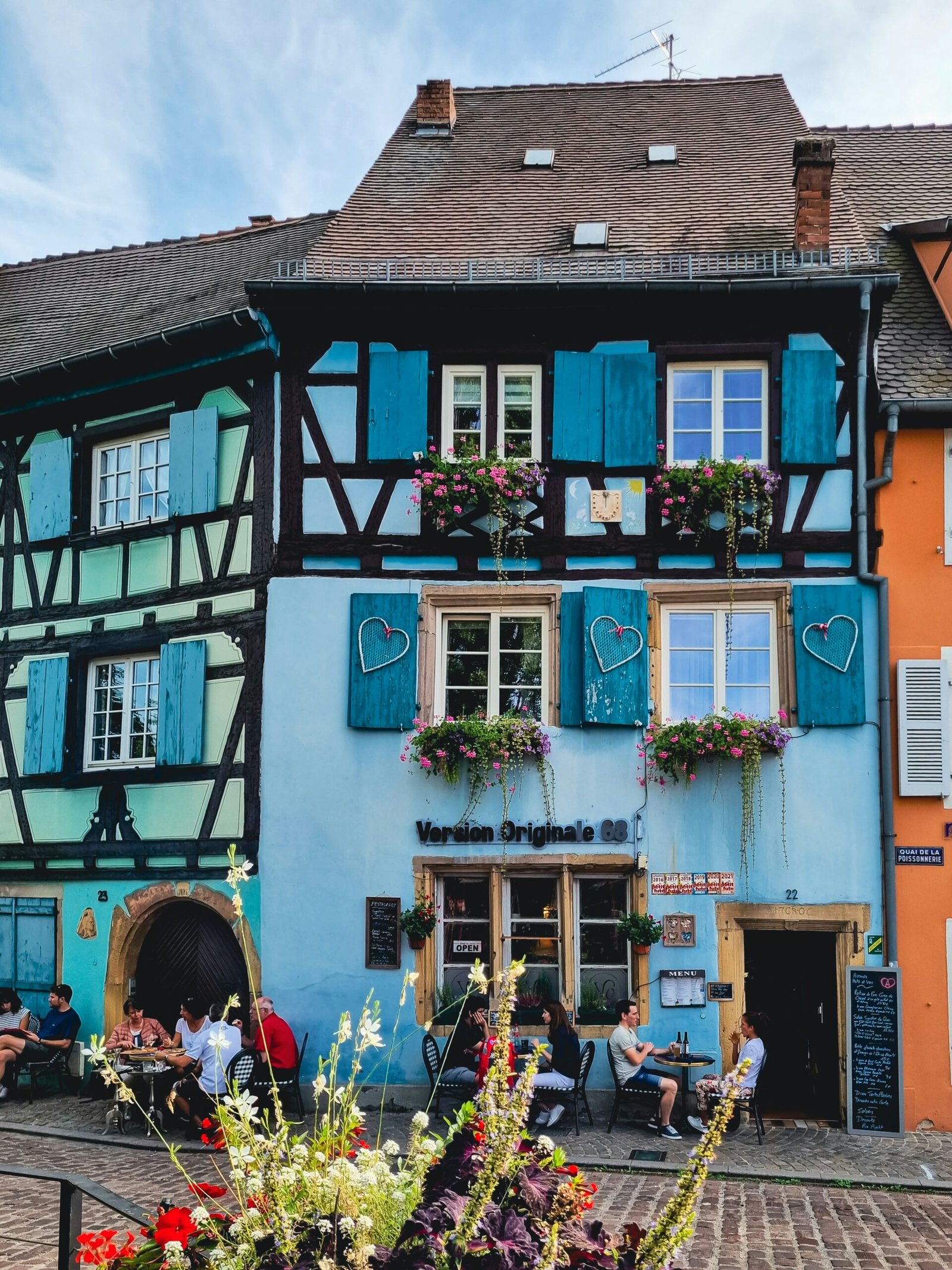 Flower-filled house in Colmar with blue shutters, creating a charming and peaceful backdrop for a France yoga retreat.