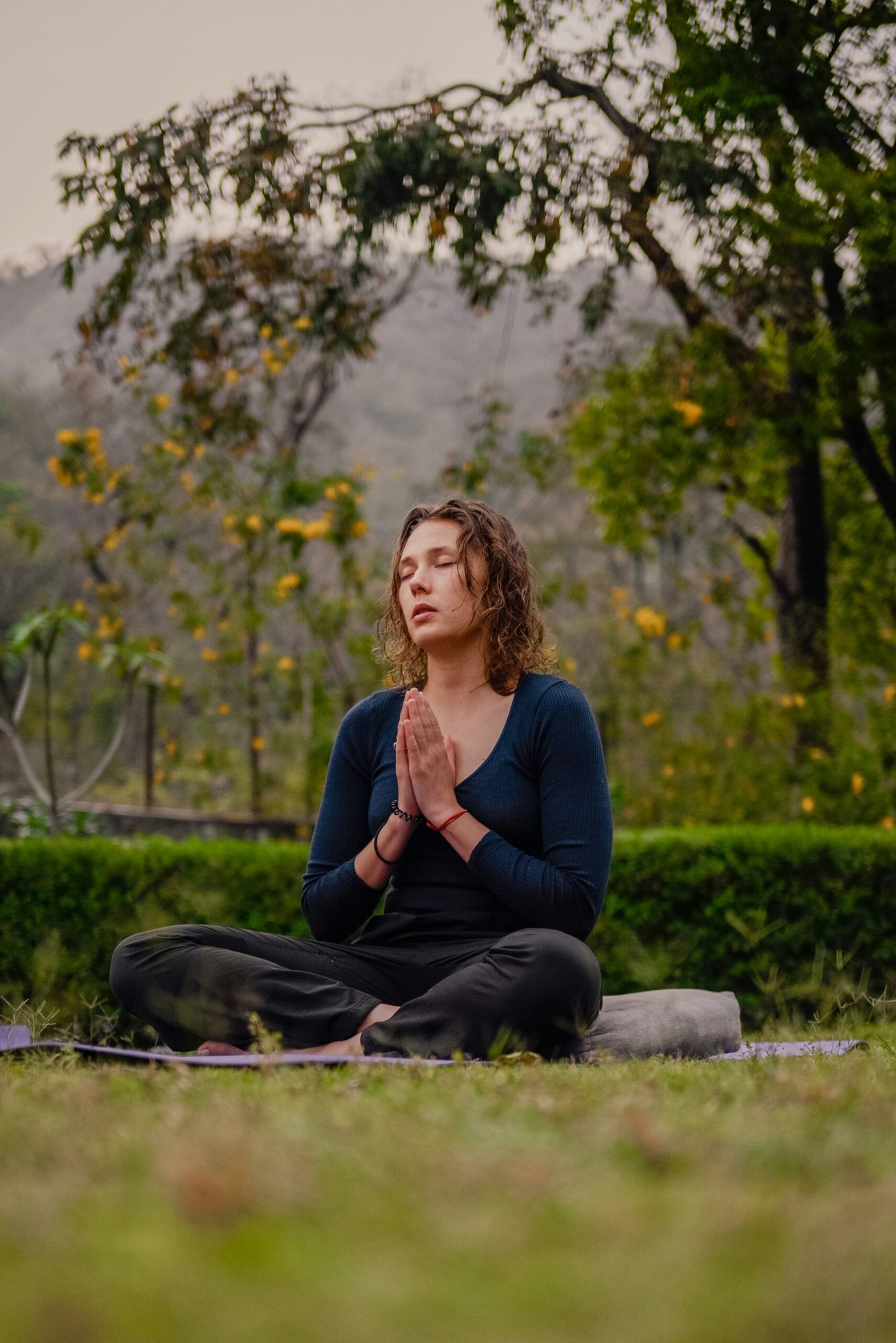A woman meditating with hands in prayer pose, illustrating simple breathwork practices to recenter during modern life stress.
