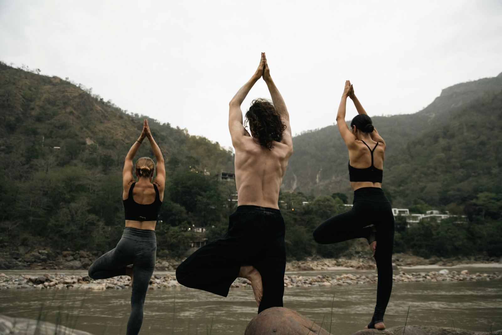 Group yoga session on riverside rocks in Rishikesh, capturing the shared practice energy of peak retreat season in India.