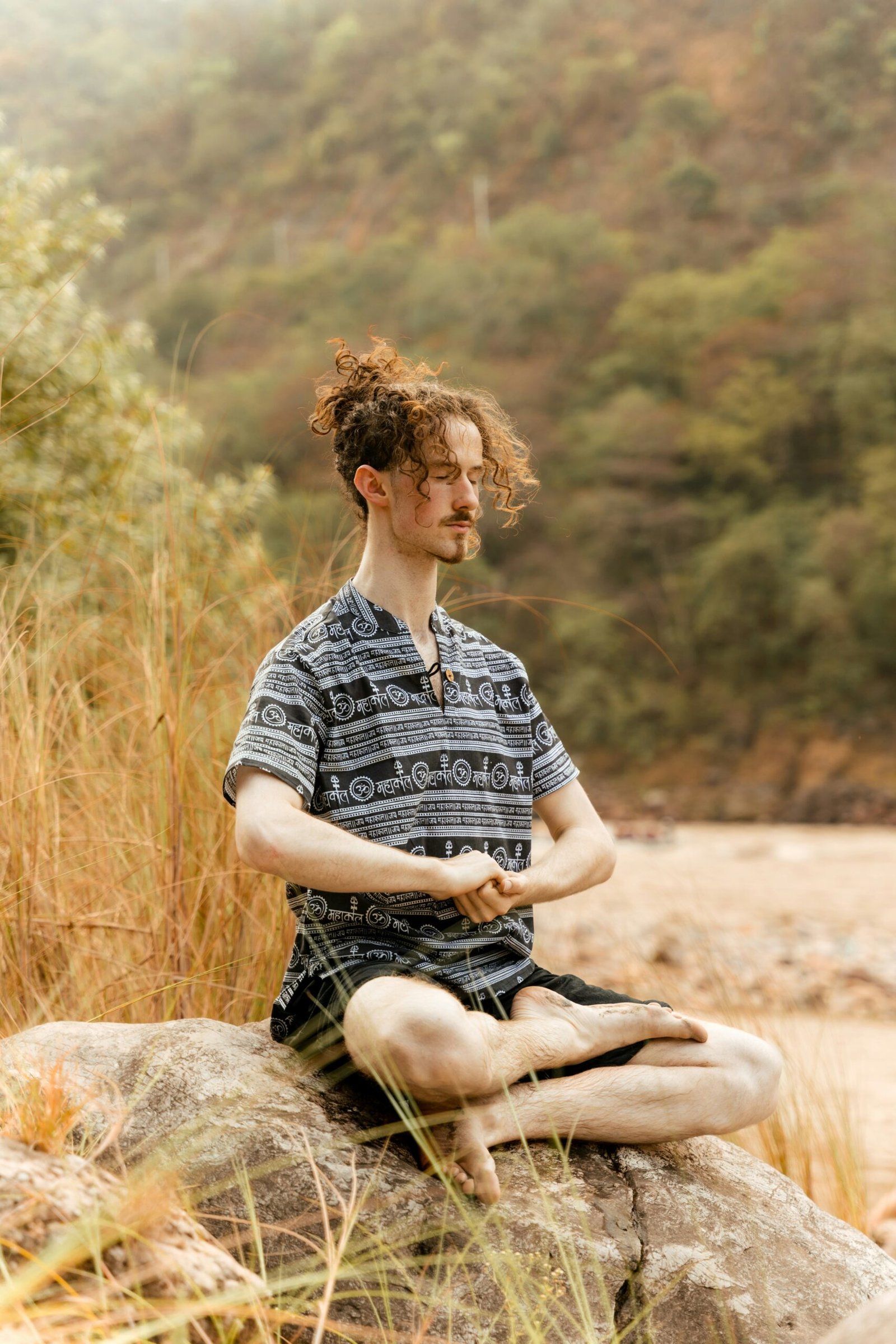 Person practicing yoga on a rock by the Ganga in Rishikesh during a peaceful retreat session.