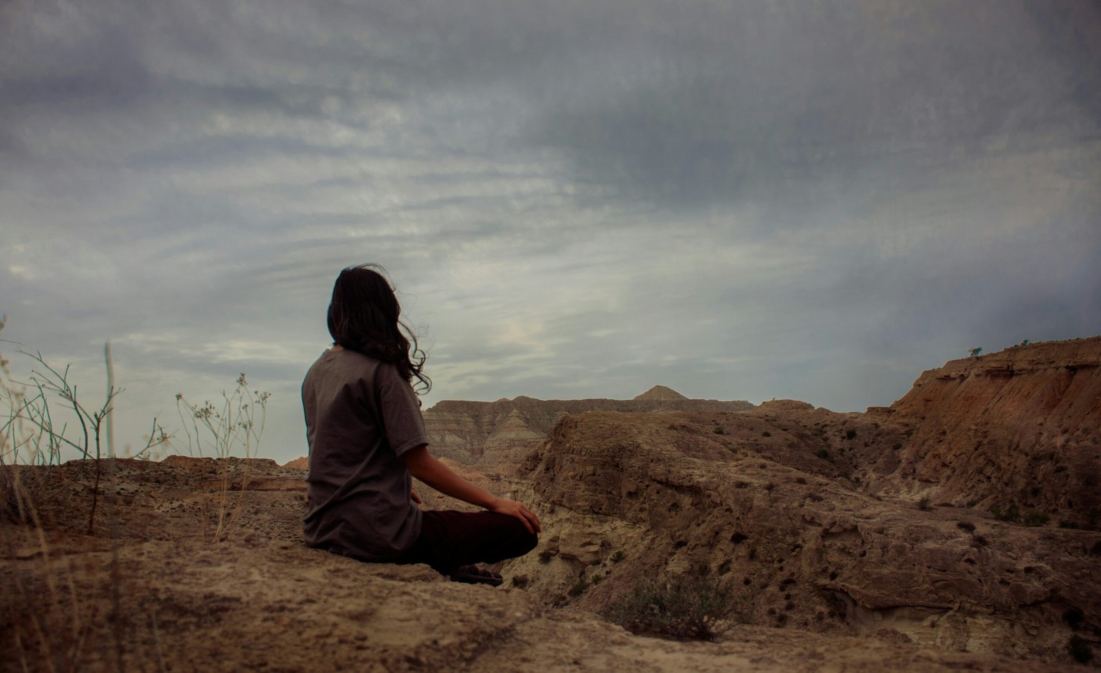 A solitary woman meditating on a desert cliff overlooking a vast canyon, representing the profound inner peace and self-connection found during a solo yoga retreat.