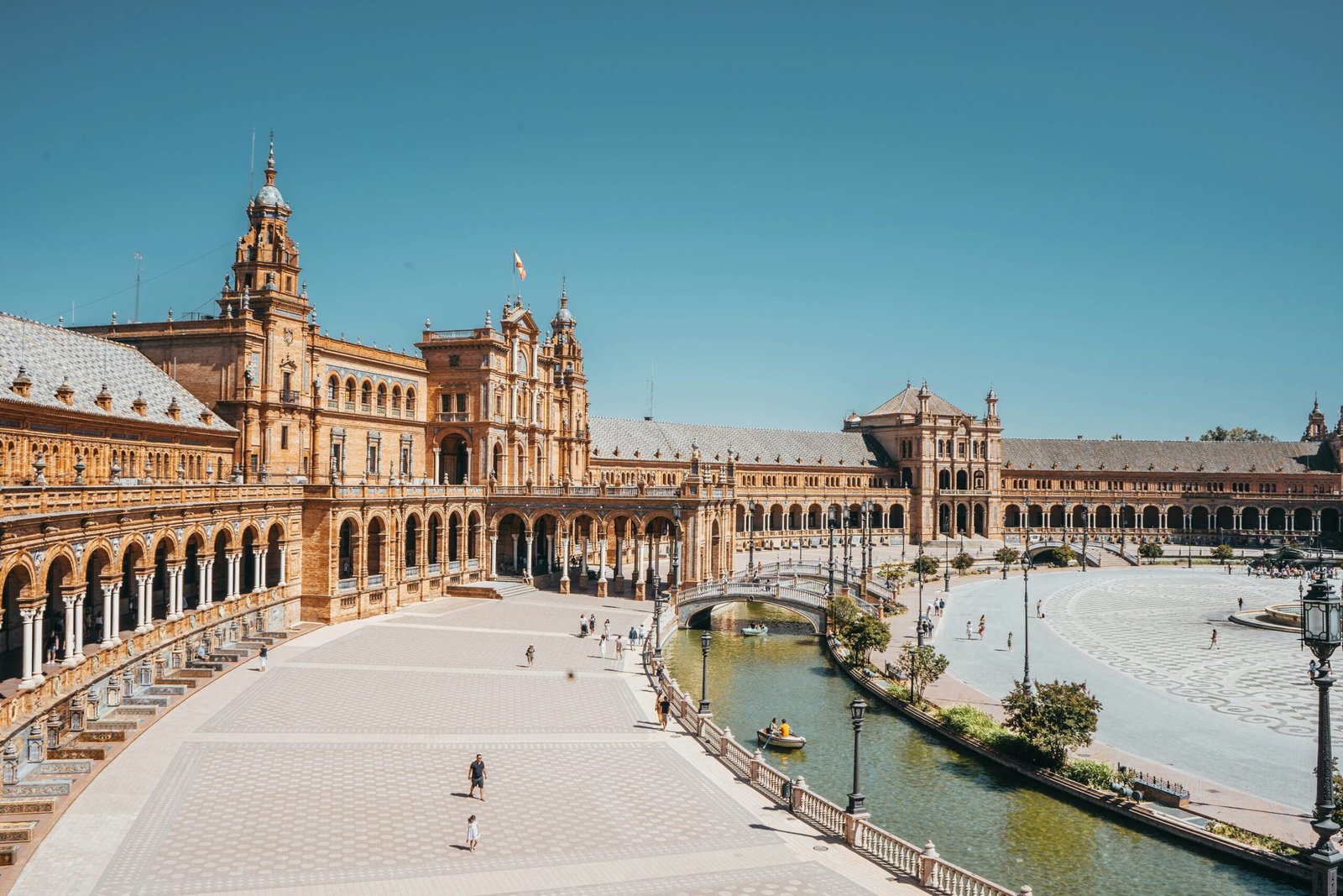 Plaza de España in Seville, Spain, with a sunlit brick tower and historic architecture under a clear blue sky.