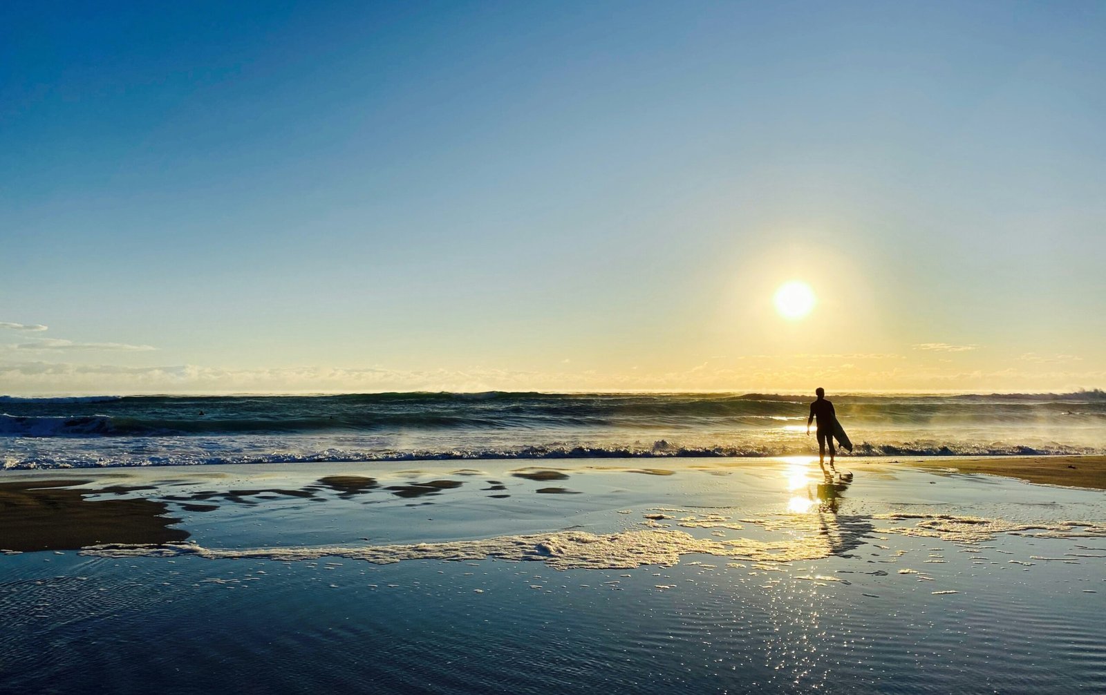A lone surfer entering the Atlantic Ocean at sunrise on a golden Portuguese beach, illustrating the surf and yoga lifestyle that defines Portugal's wellness sanctuary.