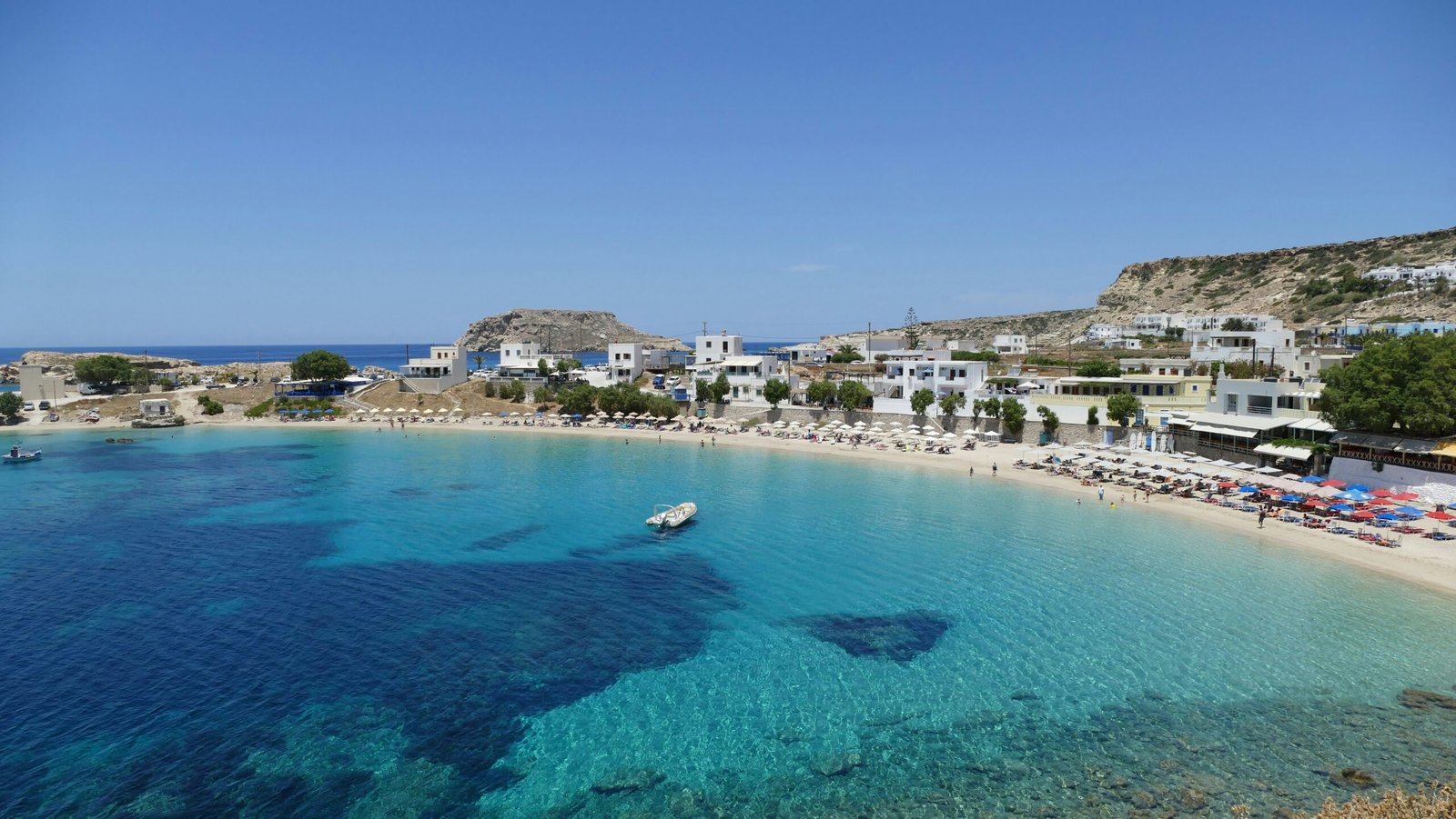 Turquoise beach and white hillside buildings in Karpathos, ideal for a warm and joyful Greece retreat by the sea.