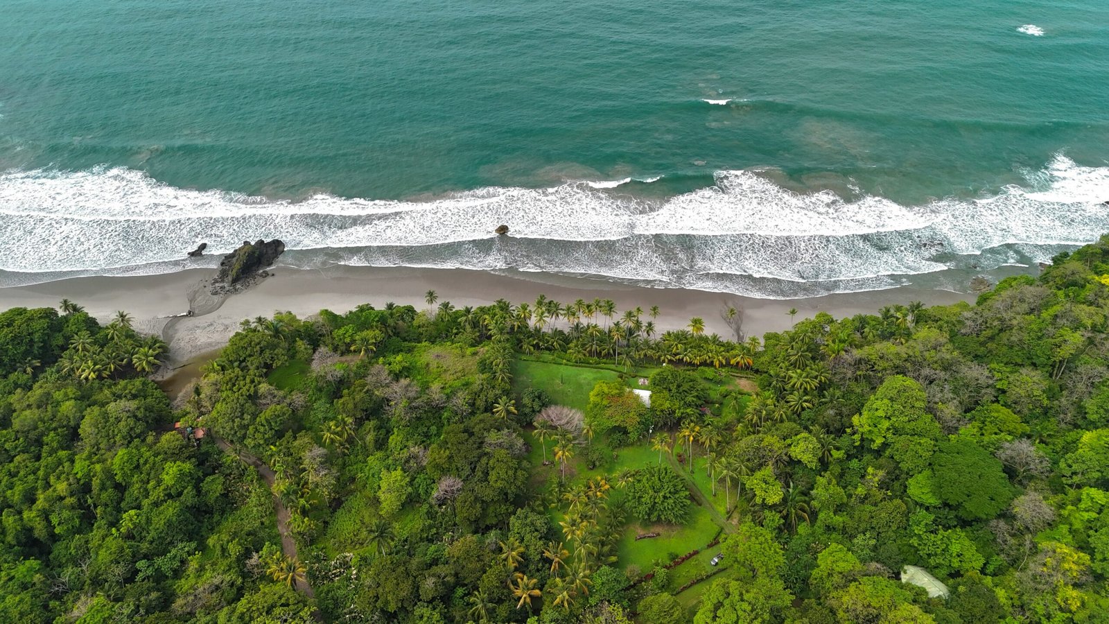 Aerial view of Manuel Antonio, Costa Rica, with bright beach, lush green forest, and blue Pacific water.