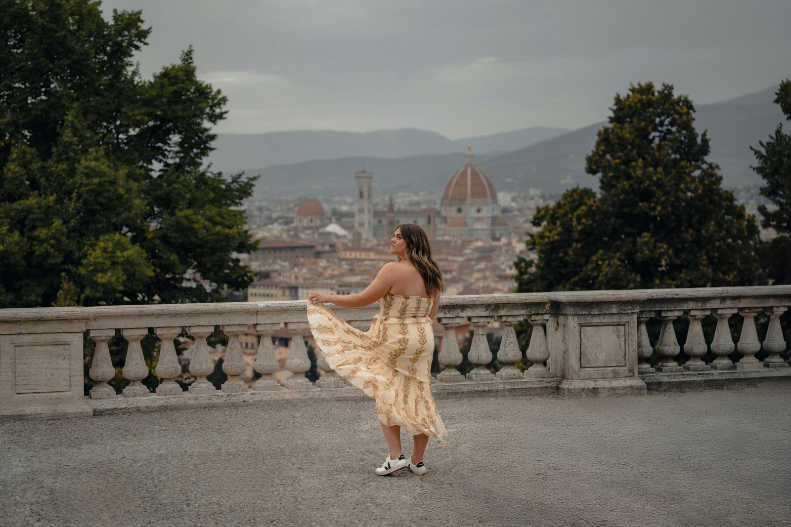 A woman in a floral dress twirling on a balcony overlooking Florence, practicing expressive movement to release stress and tension.