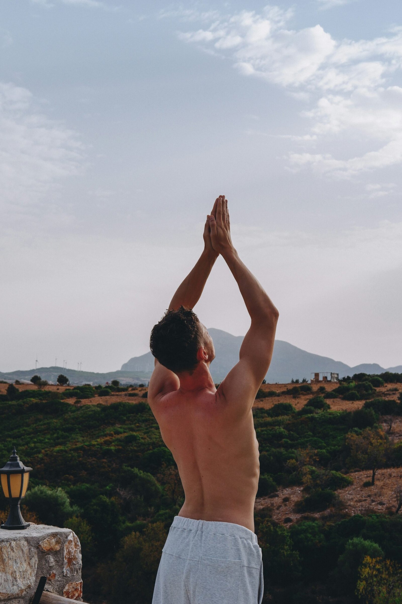 A man practicing a standing yoga pose with hands in prayer position overlooking a vast, green hilly landscape, symbolizing the connection between physical health and environmental preservation at a Portuguese eco-retreat.