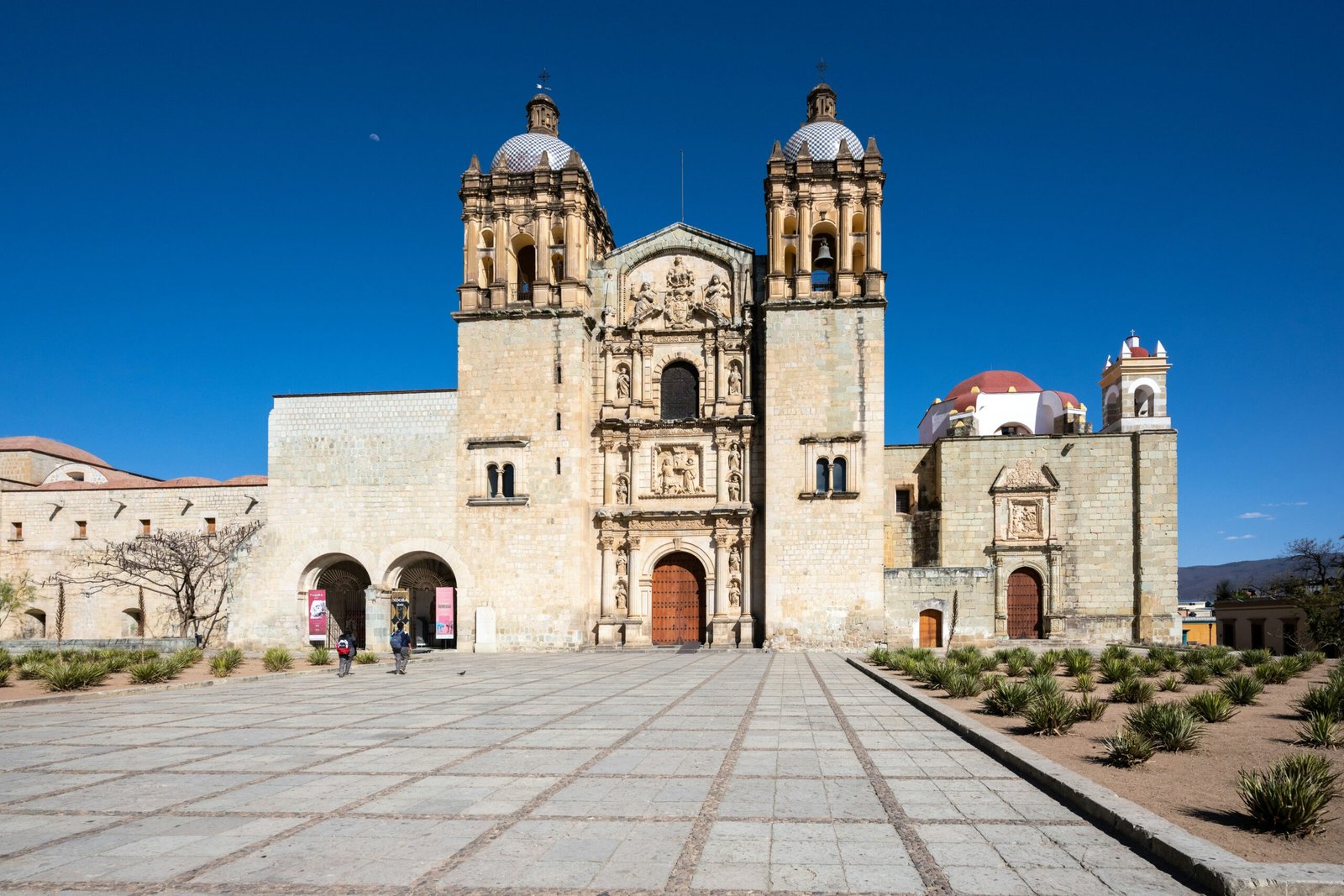 Historic church with an ornate stone facade under a bright blue sky in Oaxaca, Mexico.