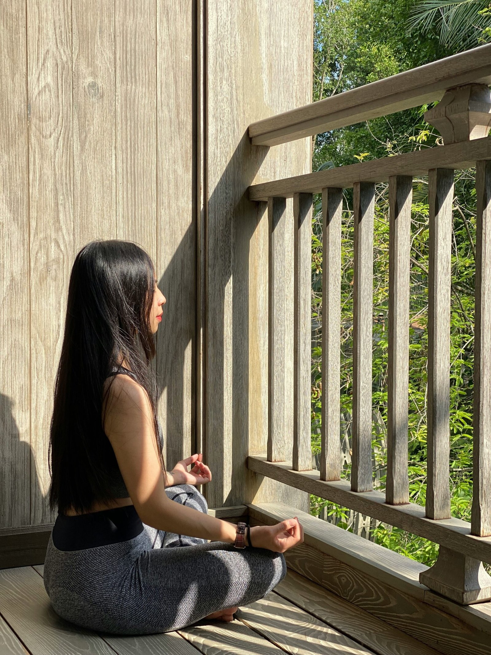 A woman practicing seated meditation on a rustic wooden balcony overlooking lush trees, capturing the peaceful solitude of a countryside yoga retreat in Alentejo, Portugal.