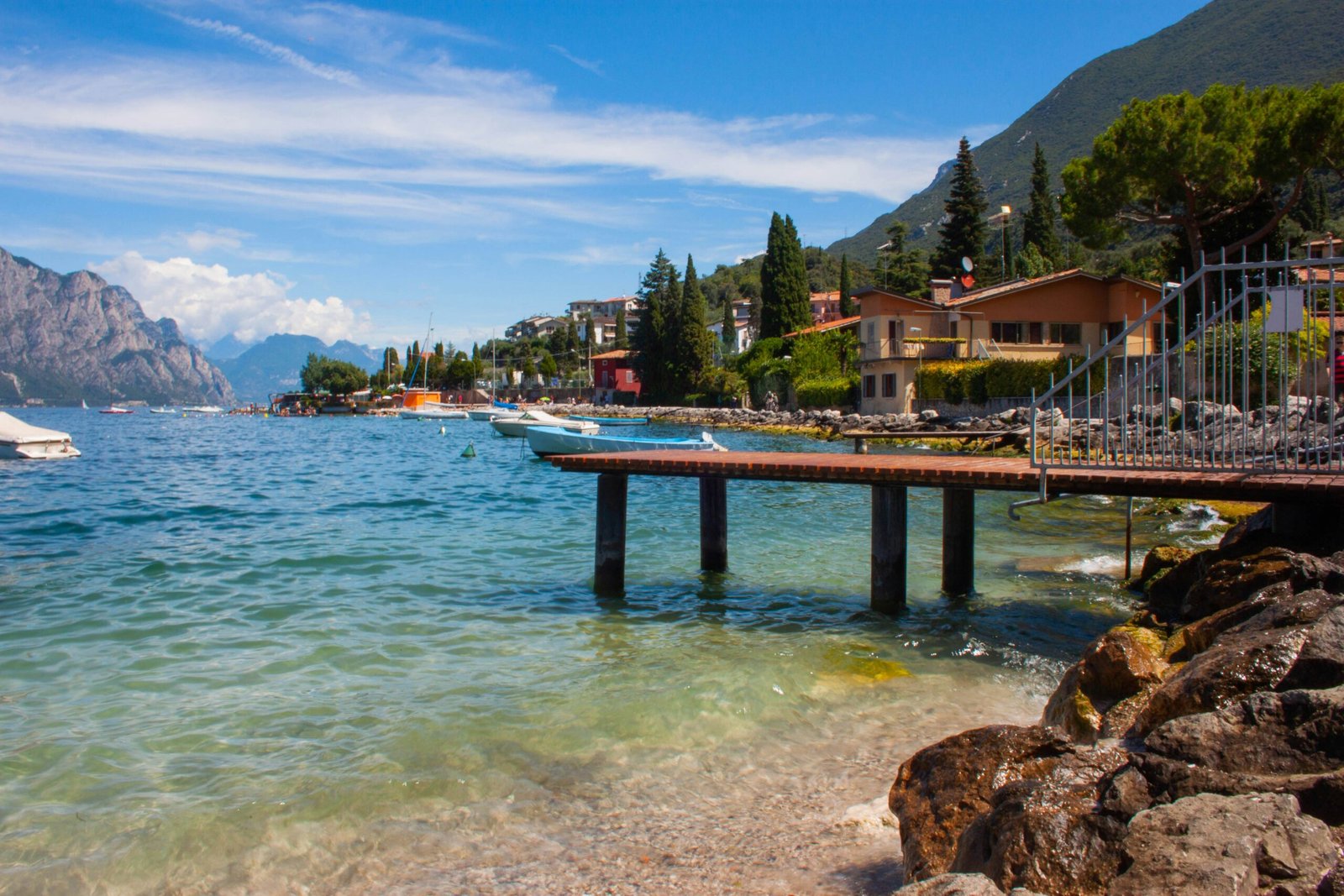Wooden dock extending into the water at Lake Garda with a bright blue sky and tranquil lakeside view.