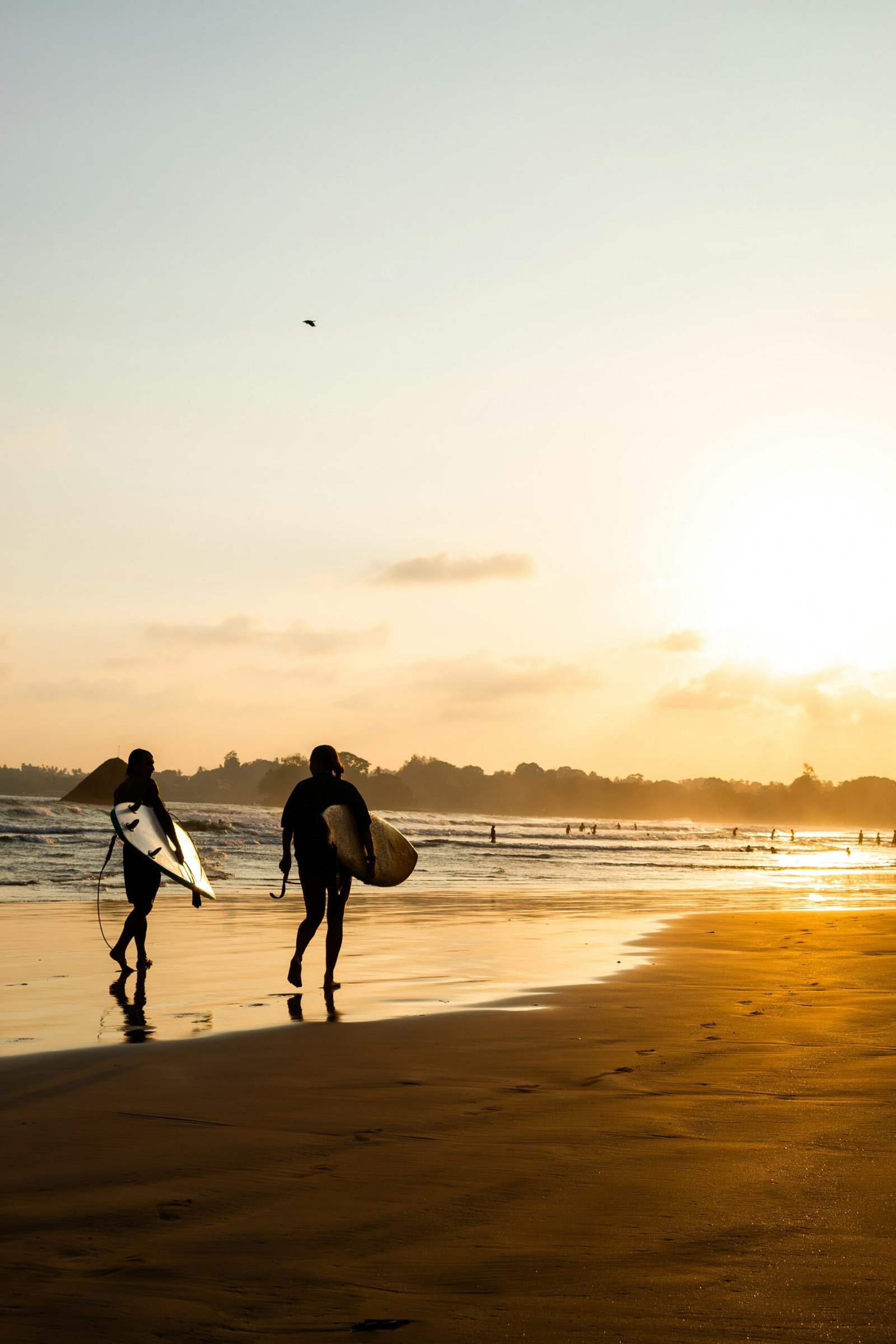 Two surfers walking along Weligama Beach in Sri Lanka, matching the vibrant and energizing feel of a winter yoga retreat by the sea.