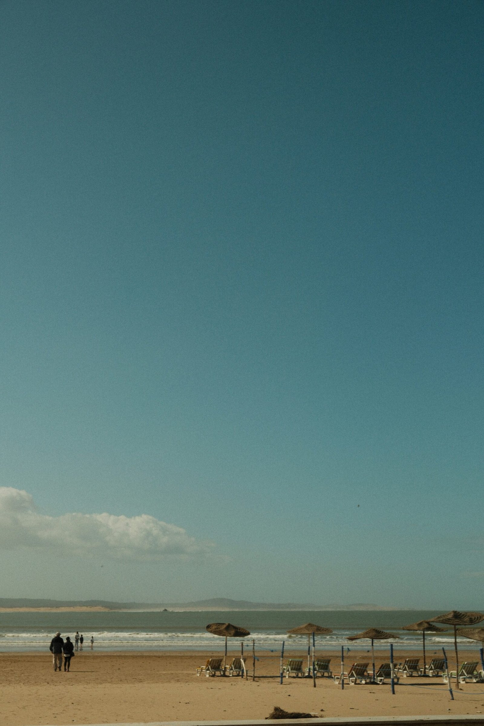 A wide sandy beach in Essaouira, Morocco, with traditional straw umbrellas and a distant view of the Atlantic coastline during a peaceful October morning.