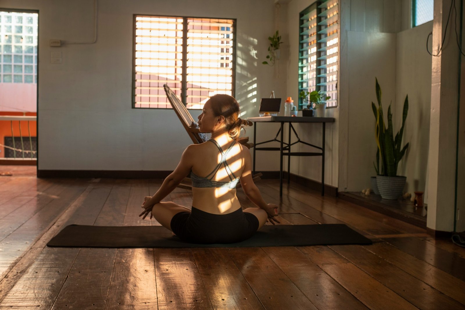 A woman practicing seated yoga on a black mat in a sunlit home studio, demonstrating how to maintain a consistent mindfulness routine after returning from a wellness retreat.