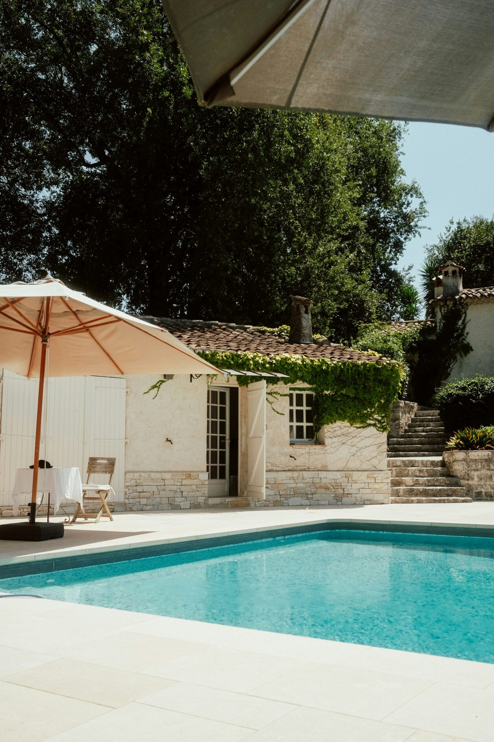 Swimming pool and patio with umbrellas and lounge seating in a sunny resort setting for a relaxing retreat stay in southern France.