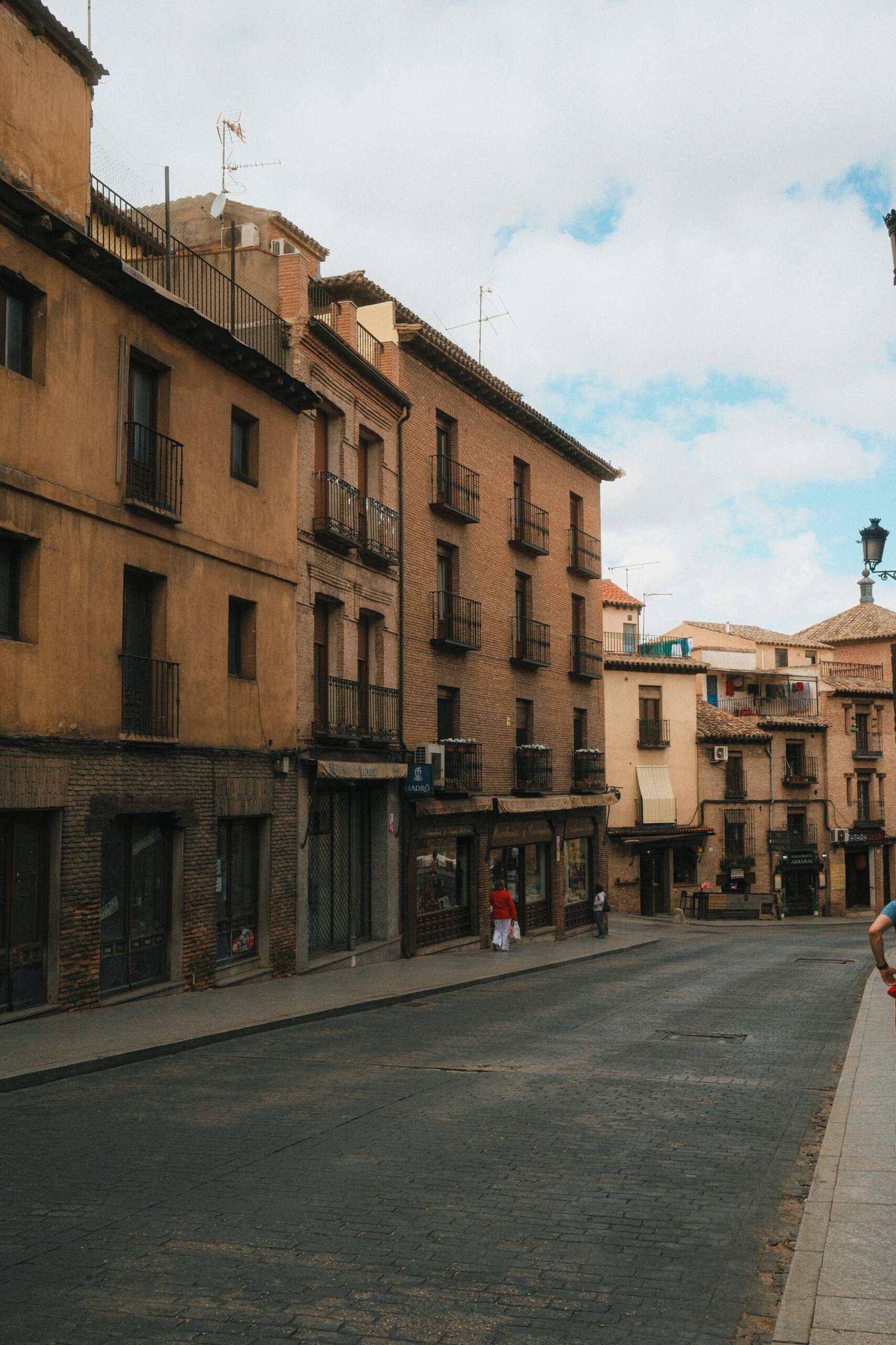Quiet old-town street in Toledo, Spain, with tall historic buildings and warm daylight.