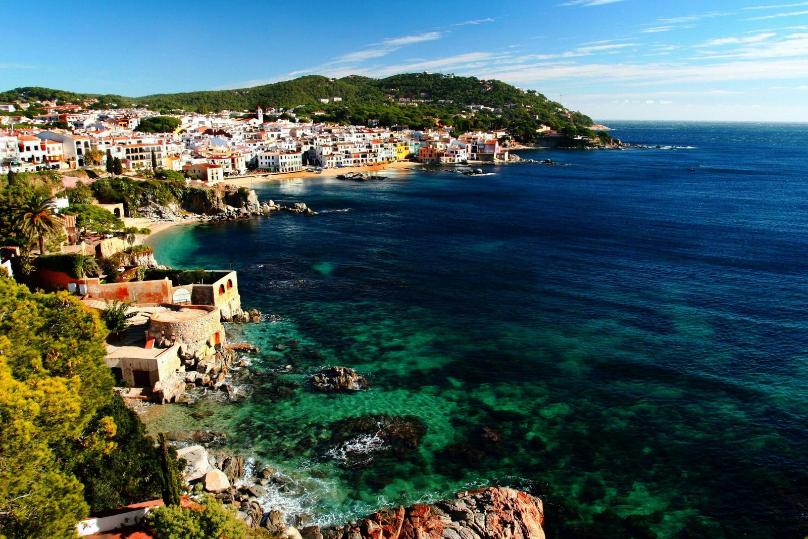 Coastal town on the Costa Brava in Catalonia, Spain, with buildings along the shoreline and rocky cliffs above the sea.