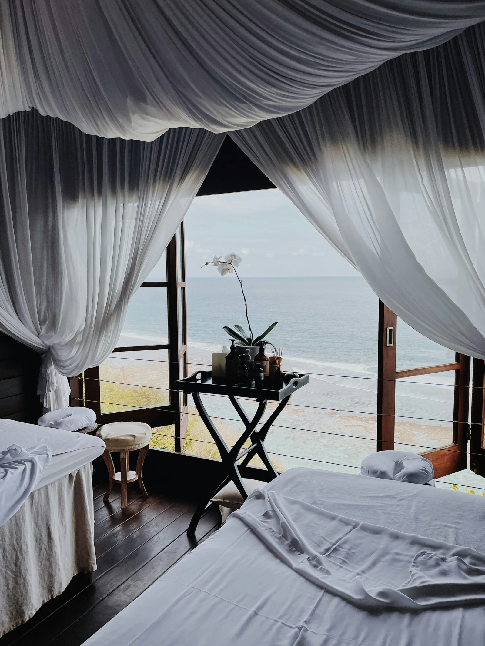 A luxury oceanfront spa treatment room with massage tables and white orchids, highlighting the emphasis on pampering and self-care in a high-end wellness retreat.