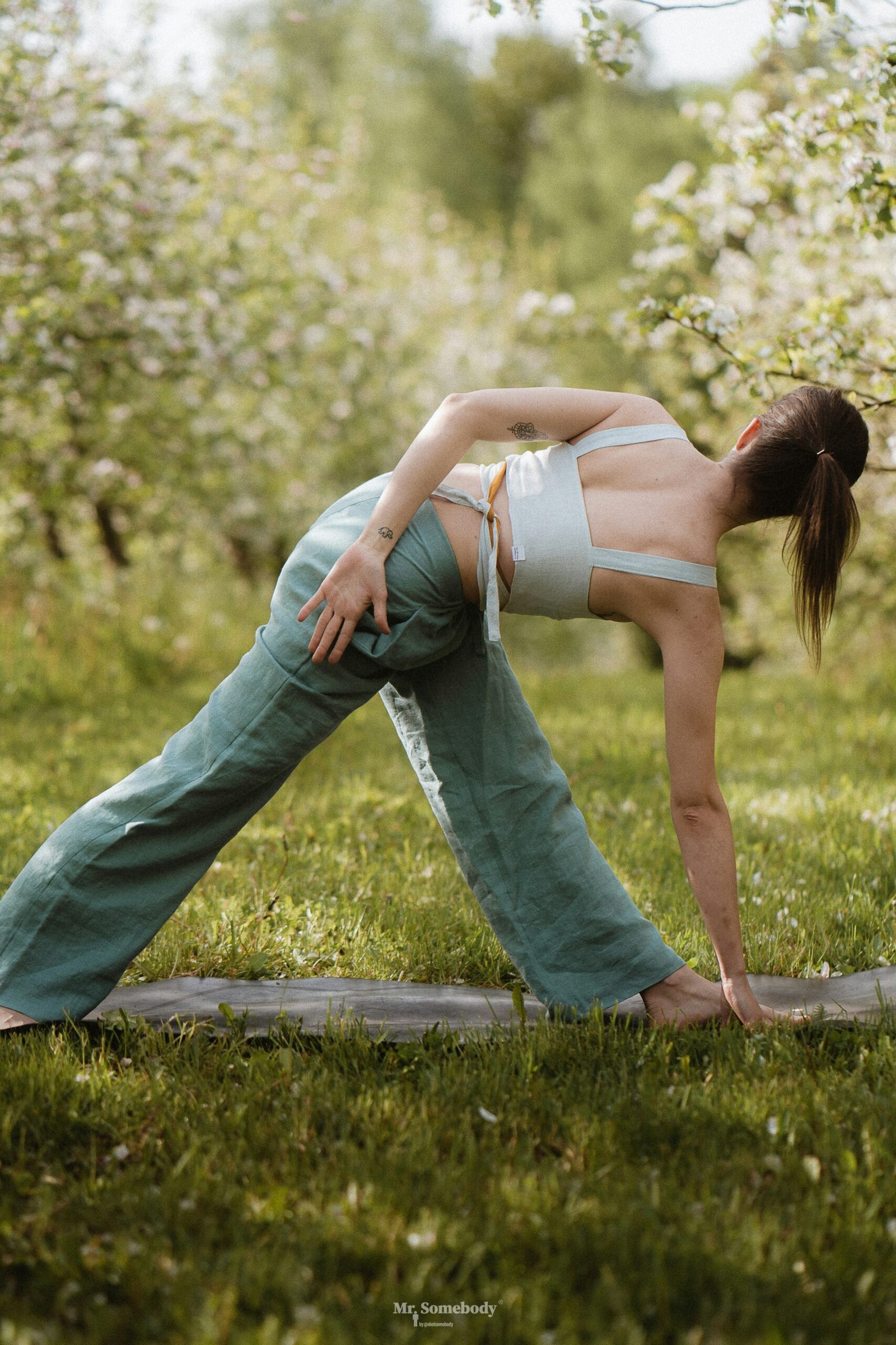 Person resting on a wooden bench in a garden during an outdoor yoga session, with a mat and soft linen nearby.