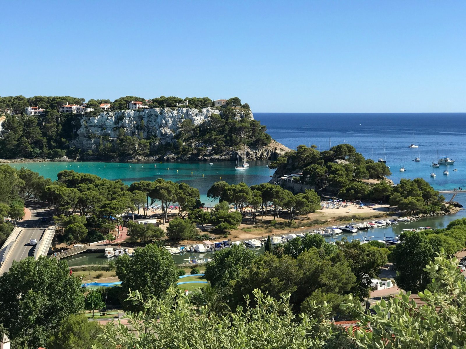 Coastal town in Menorca, Spain, with rocky shoreline and bright summer sea views.