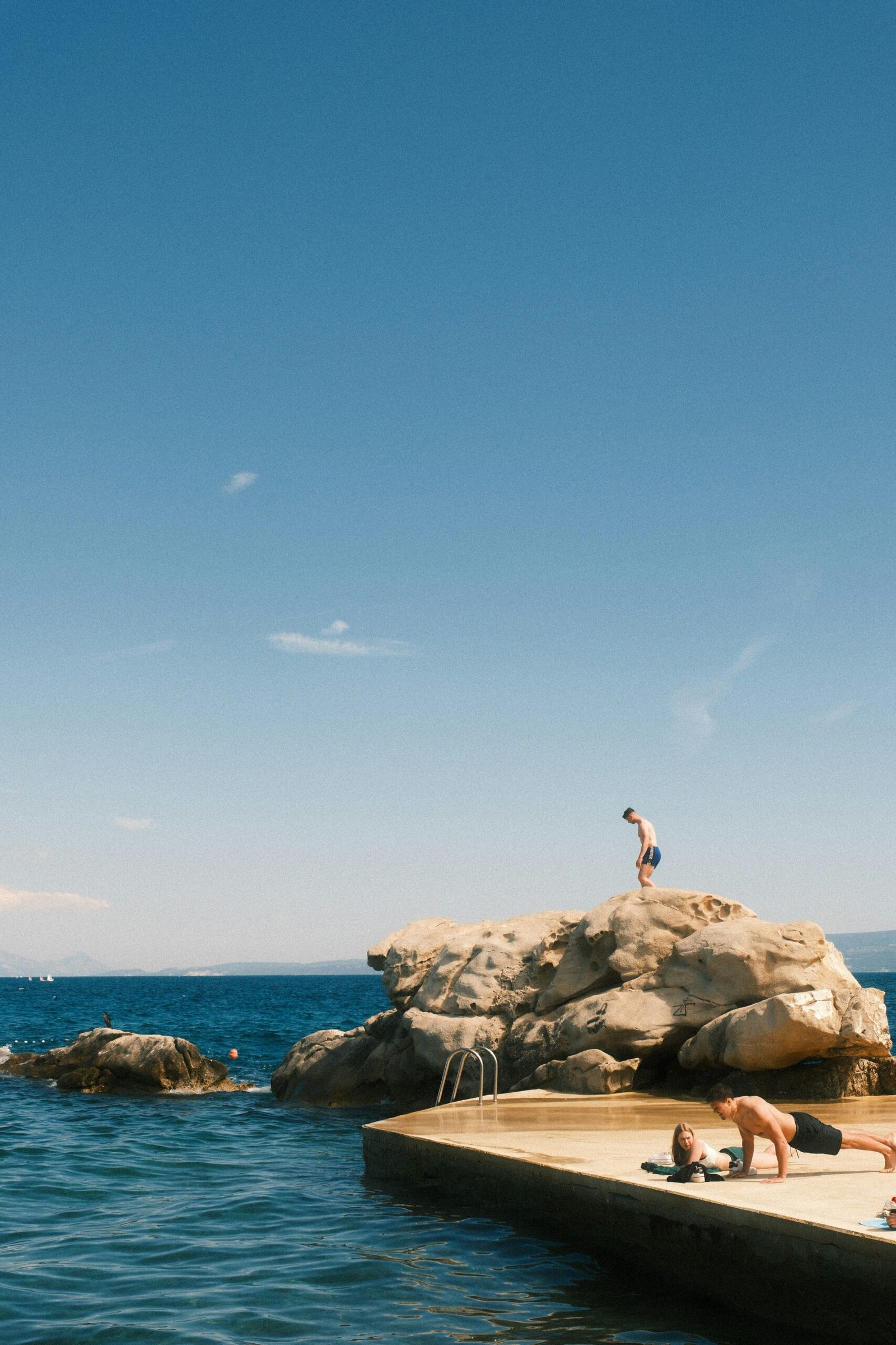 Man standing on a large coastal rock, preparing to jump into the sea.