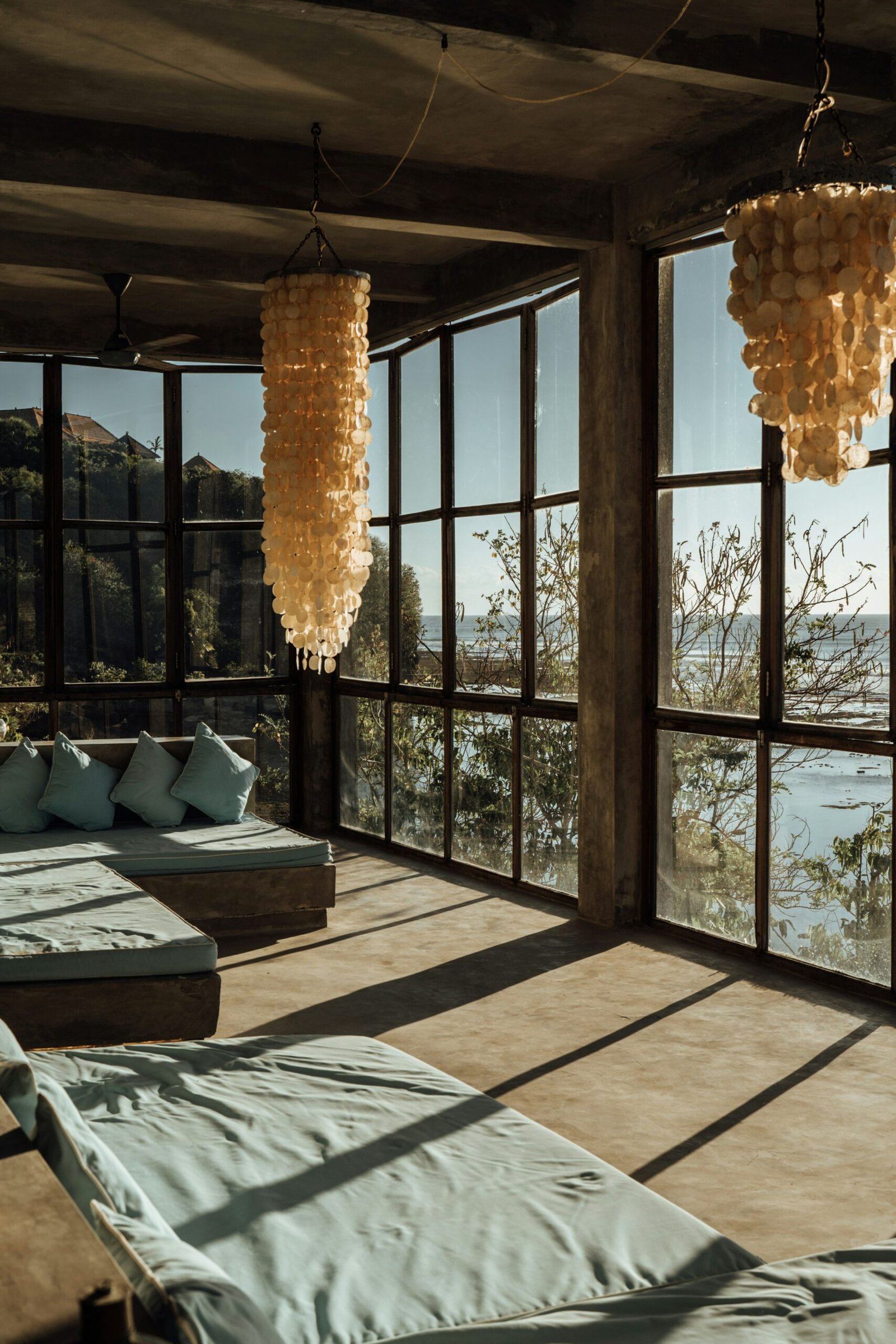 Sunlit Bali wellness room with large windows, a chandelier, and an ocean-view villa feel.