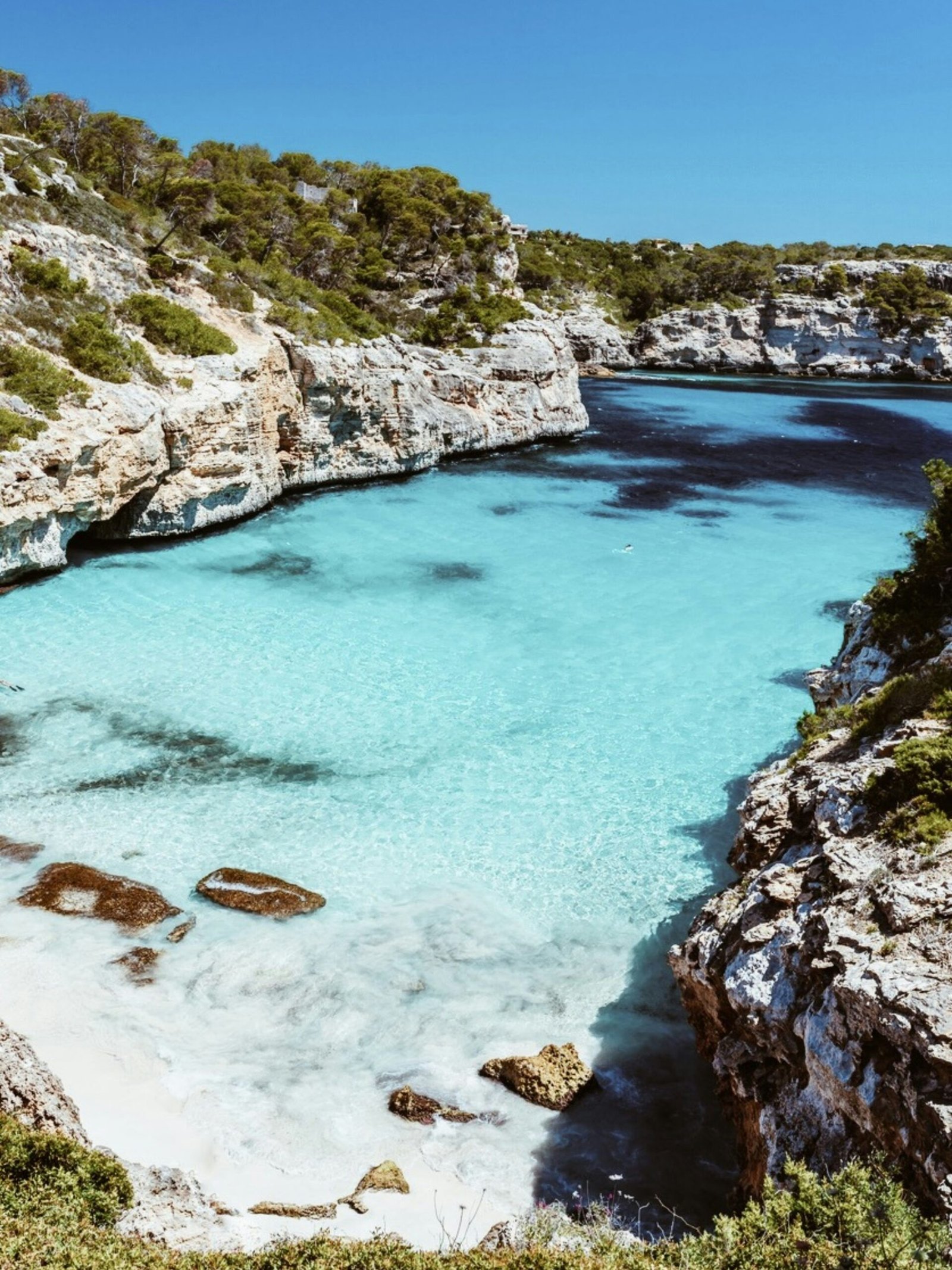 Beach between cliffs at Cala des Moro in Mallorca, Spain, with turquoise water and a narrow sandy cove.