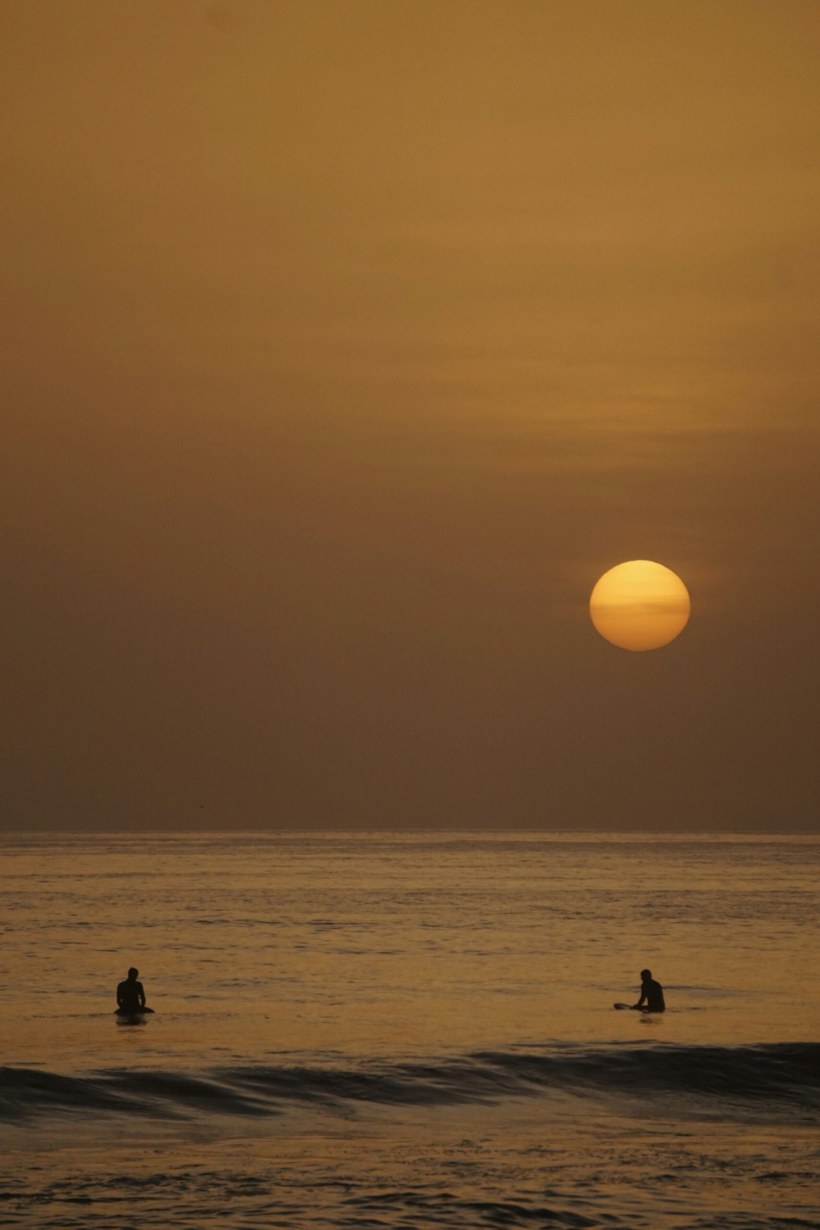 Two surfers sitting on their boards in the Atlantic Ocean at sunset in Morocco, capturing the calm and meditative atmosphere of a spring surf and yoga retreat.