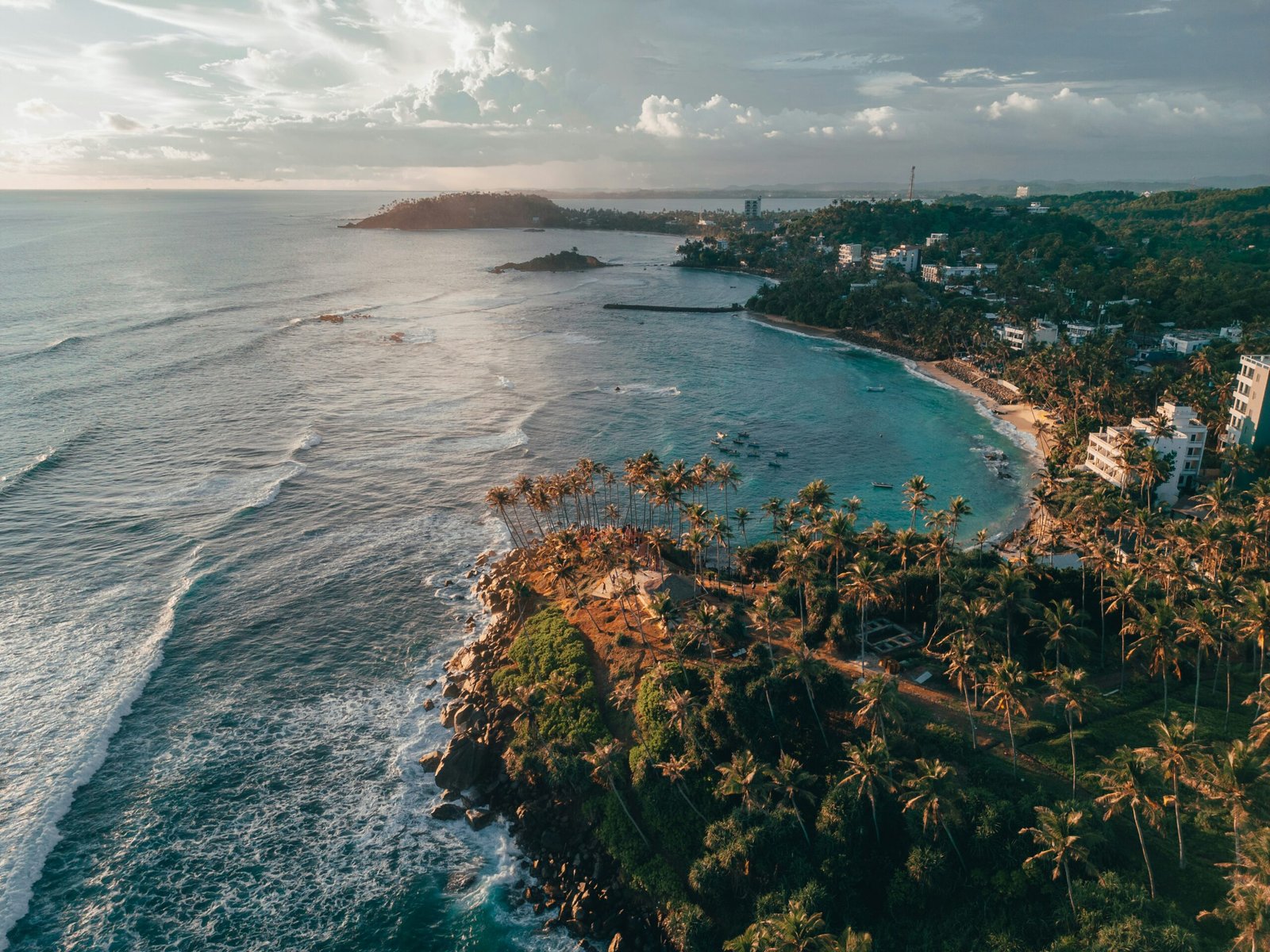 Aerial coastline view over Mirissa Beach with turquoise water and palms in southern Sri Lanka.