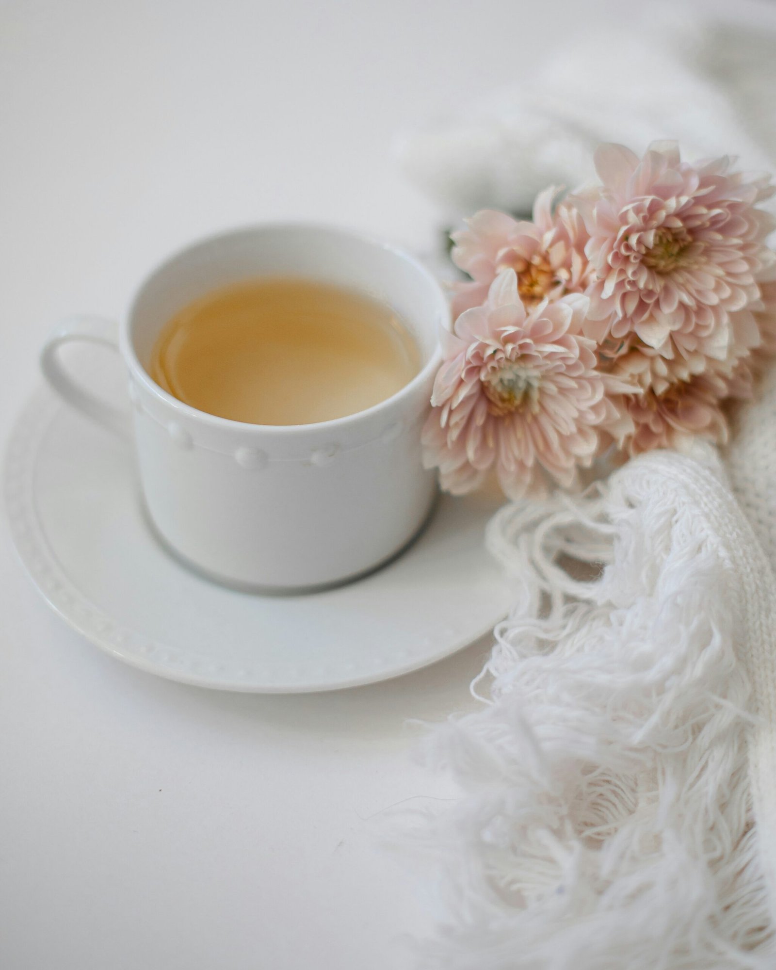 Cup of tea styled with pink flowers and white fabric in a soft, minimalist wellness still life.