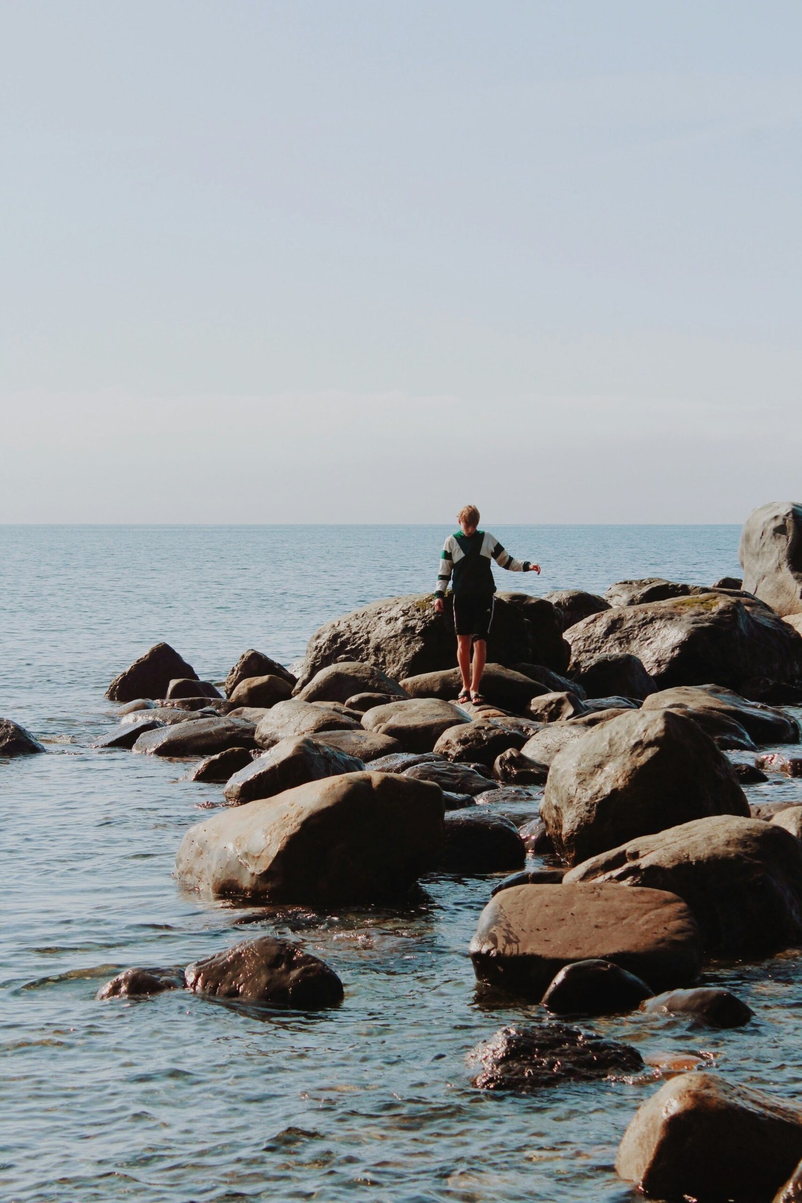 Person standing on a rock in calm water, creating a quiet and reflective wellness scene.