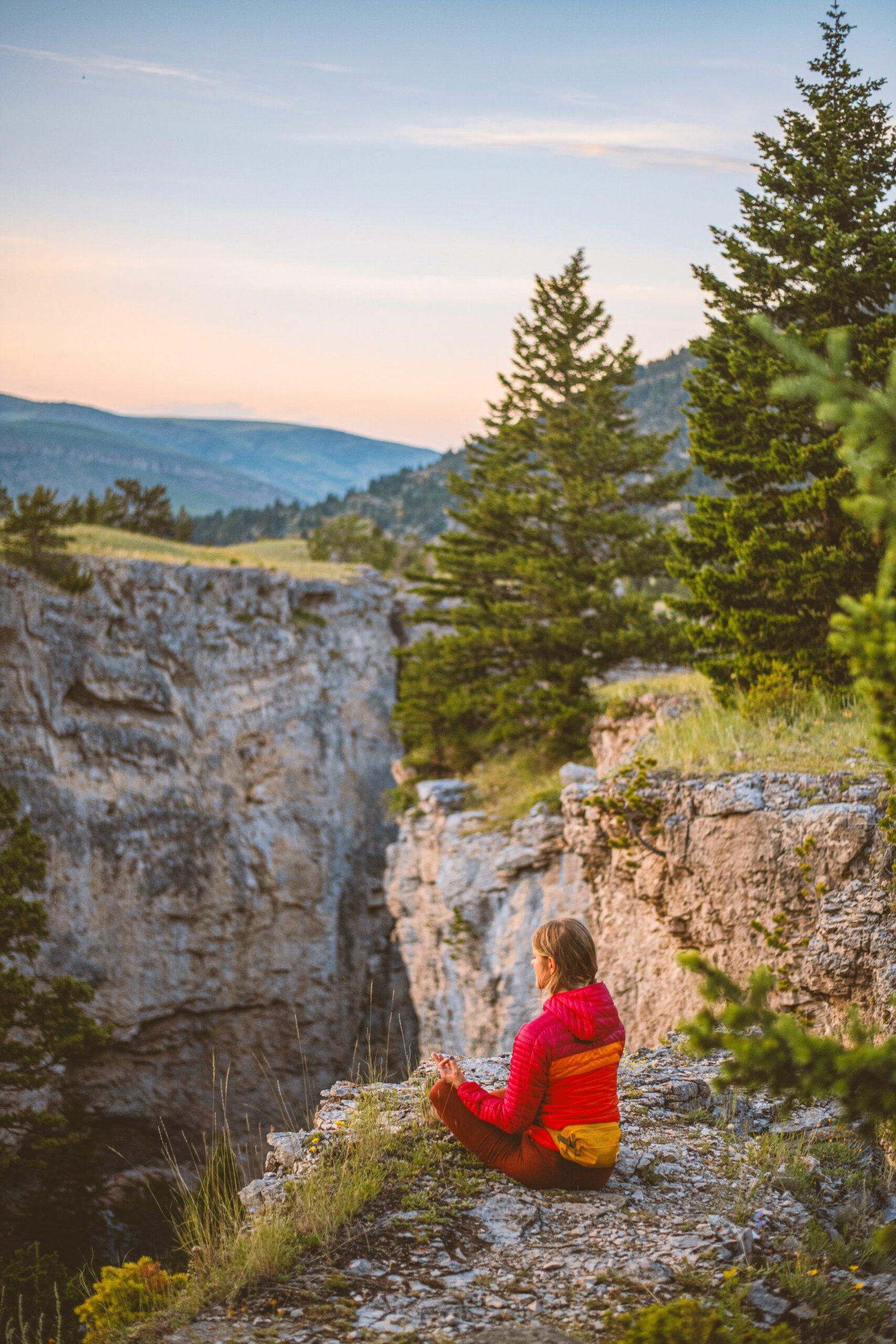 A woman practicing seated meditation on a rocky mountain ledge at sunset, representing the 'Introspective Mindset' found at wilderness yoga retreats in Northern Spain.